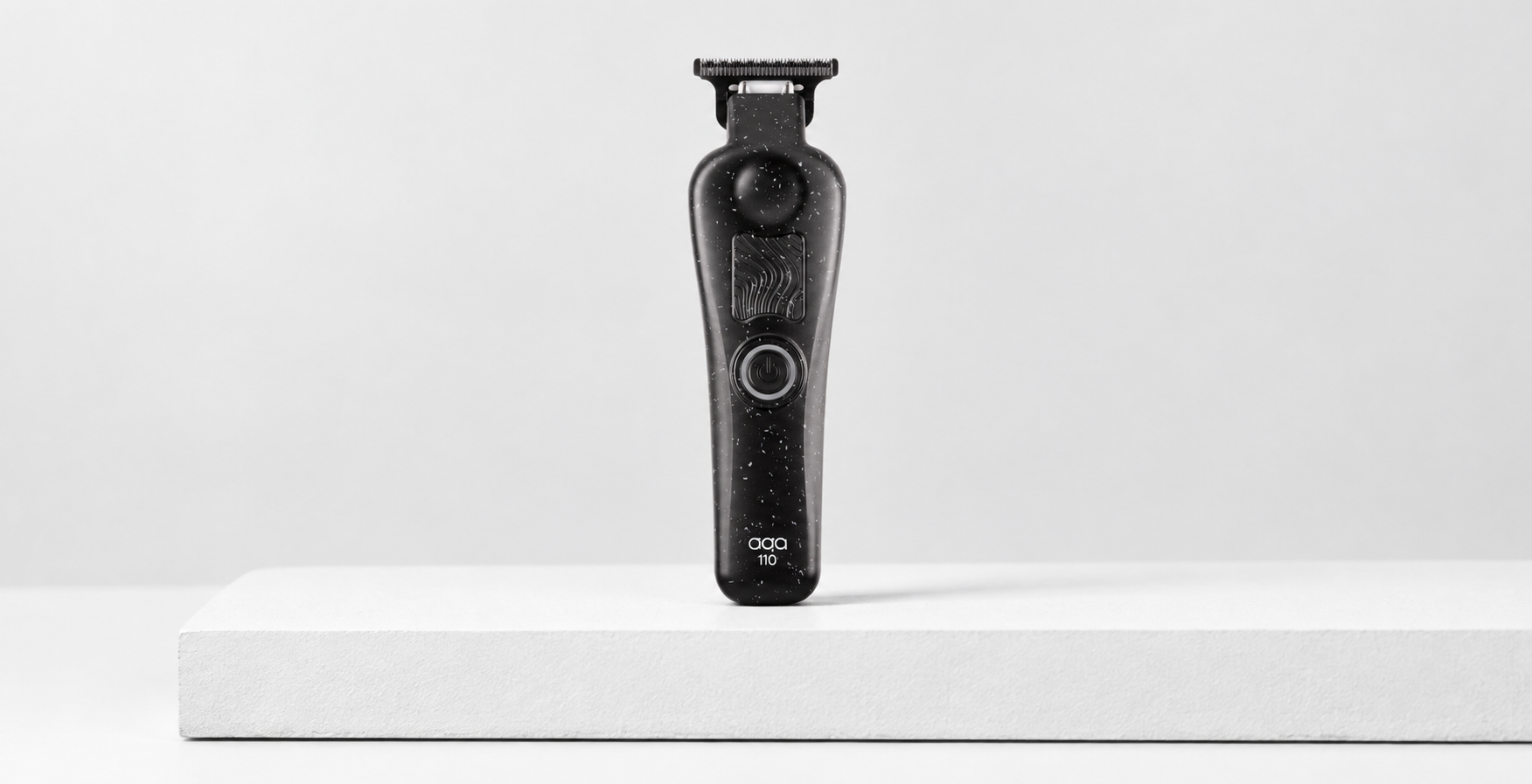 A black electric hair trimmer with a speckled star pattern stands on a white rectangular platform against a plain white background.