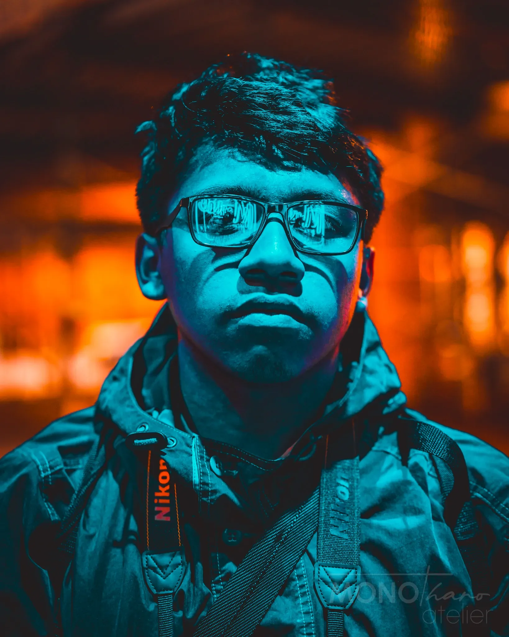 Porträt eines jungen Mannes mit Brille, dunklem Haar, in einer dunklen, urbanen Umgebung mit warmem Licht.