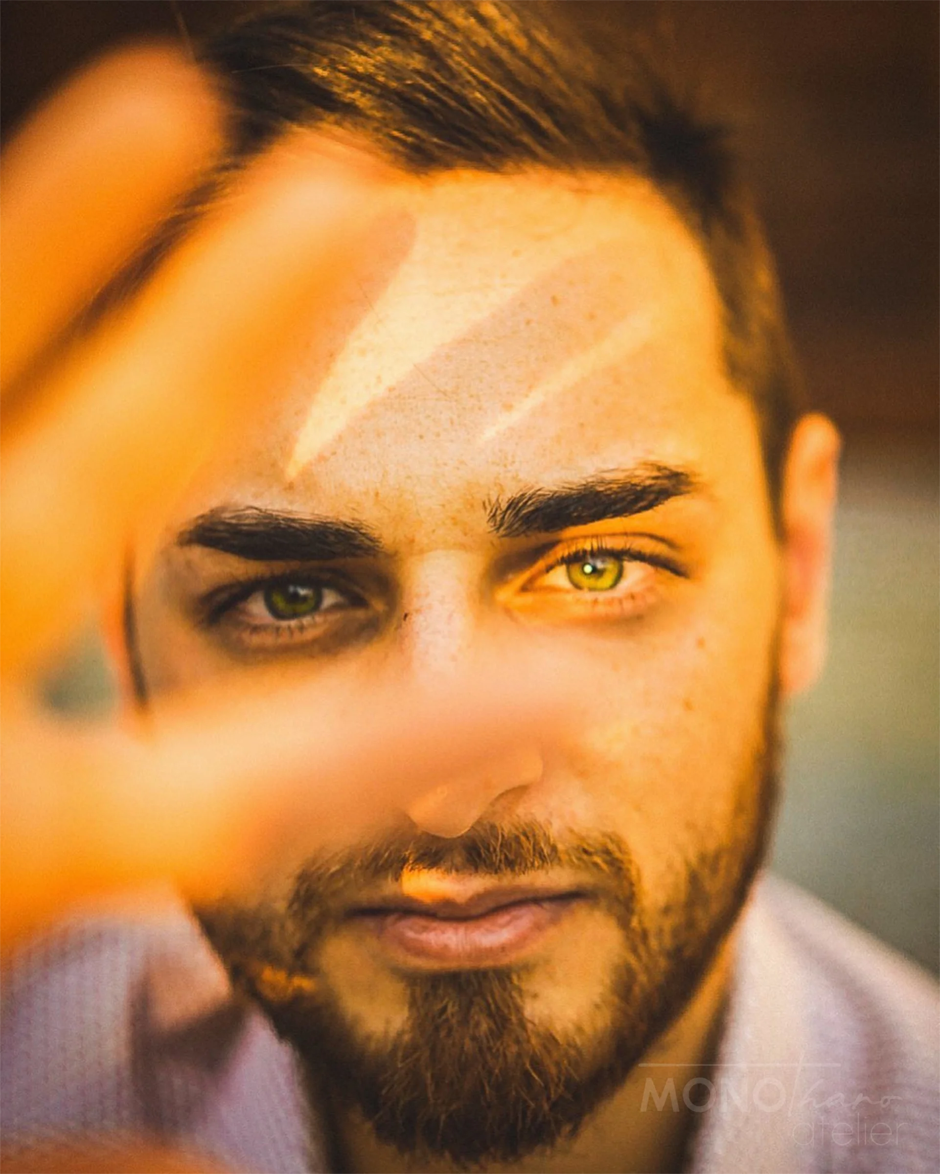 Nahaufnahme eines Mannes mit grünen Augen, braunen Haaren und Bart, der eine Hand über die Stirn hebt.