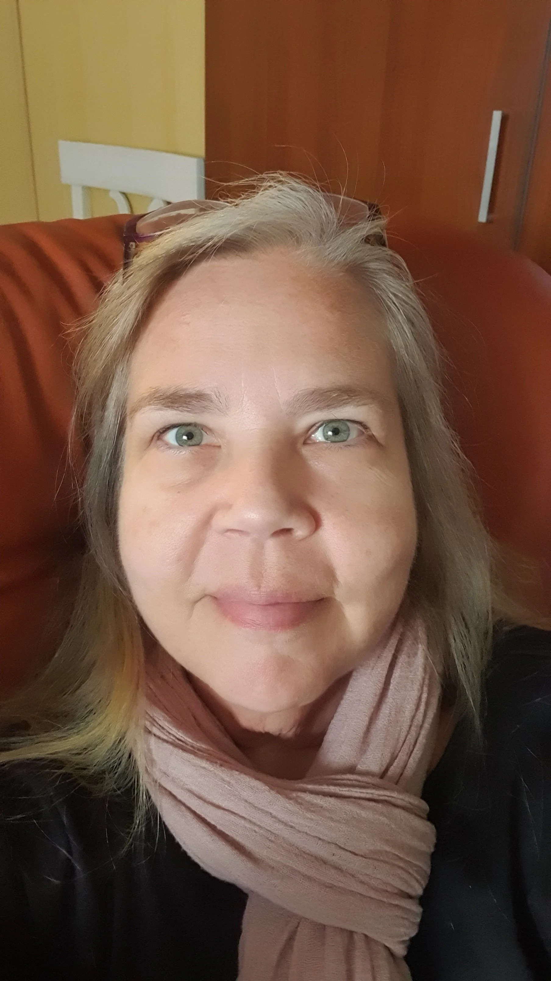 Nainen ottaa selfietä sisätiloissa, jonka taustalla on puinen seinä ja ruokapöytä.