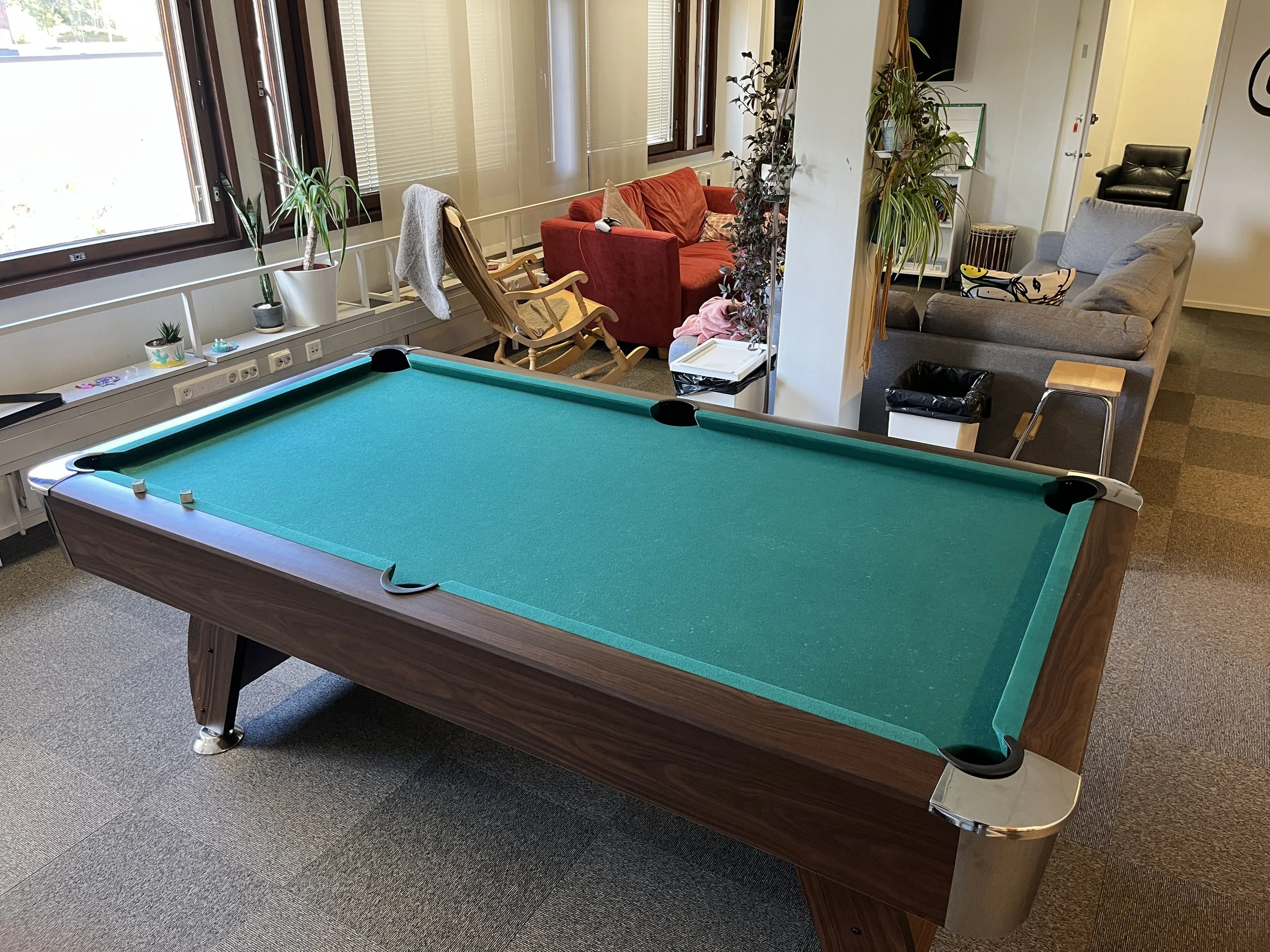 Snooker pöytä ja olohuone, jossa on sohvia, nojatuoli ja useita sisäkasveja.