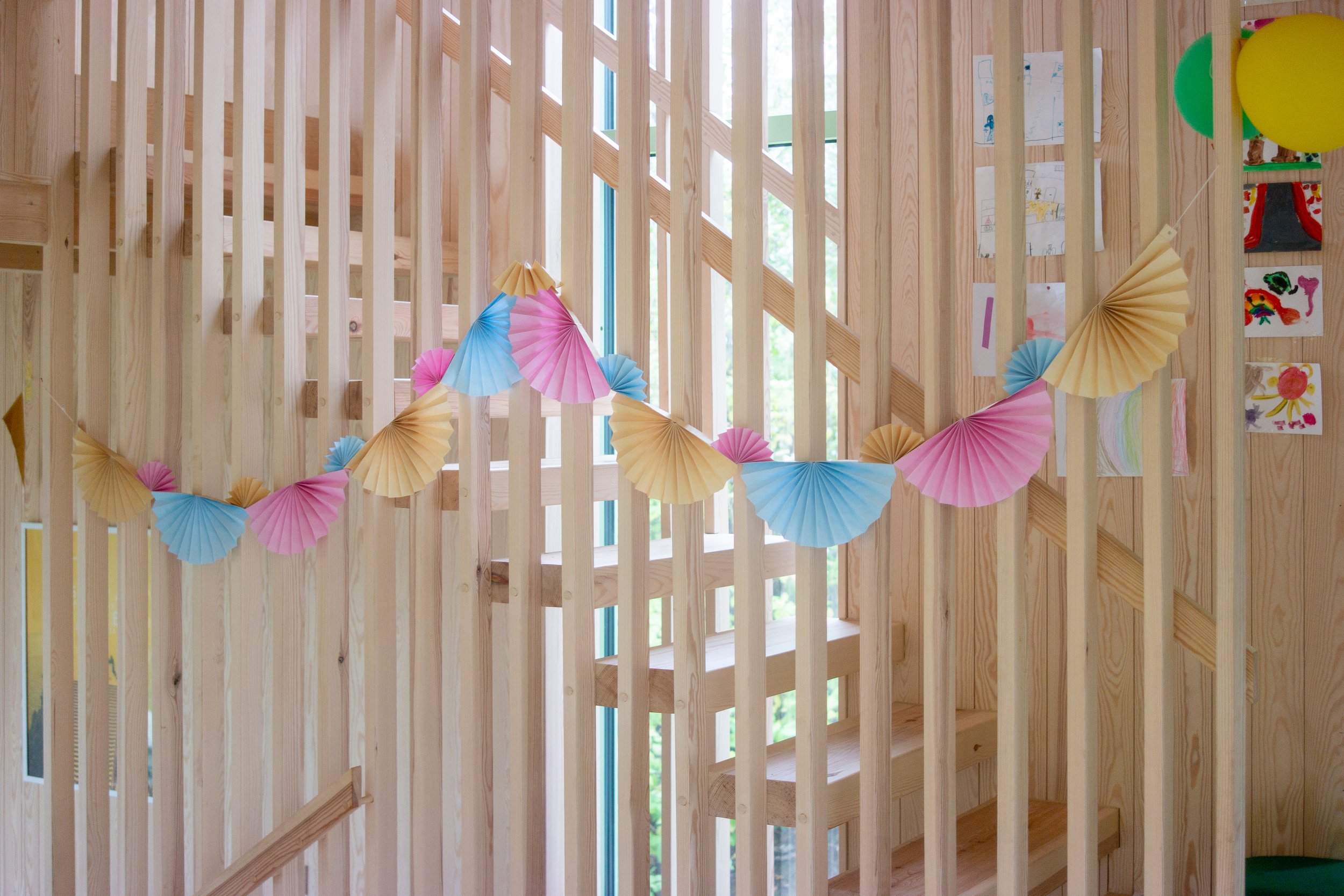 Wooden interior wall with colorful paper fans and children's drawings attached.