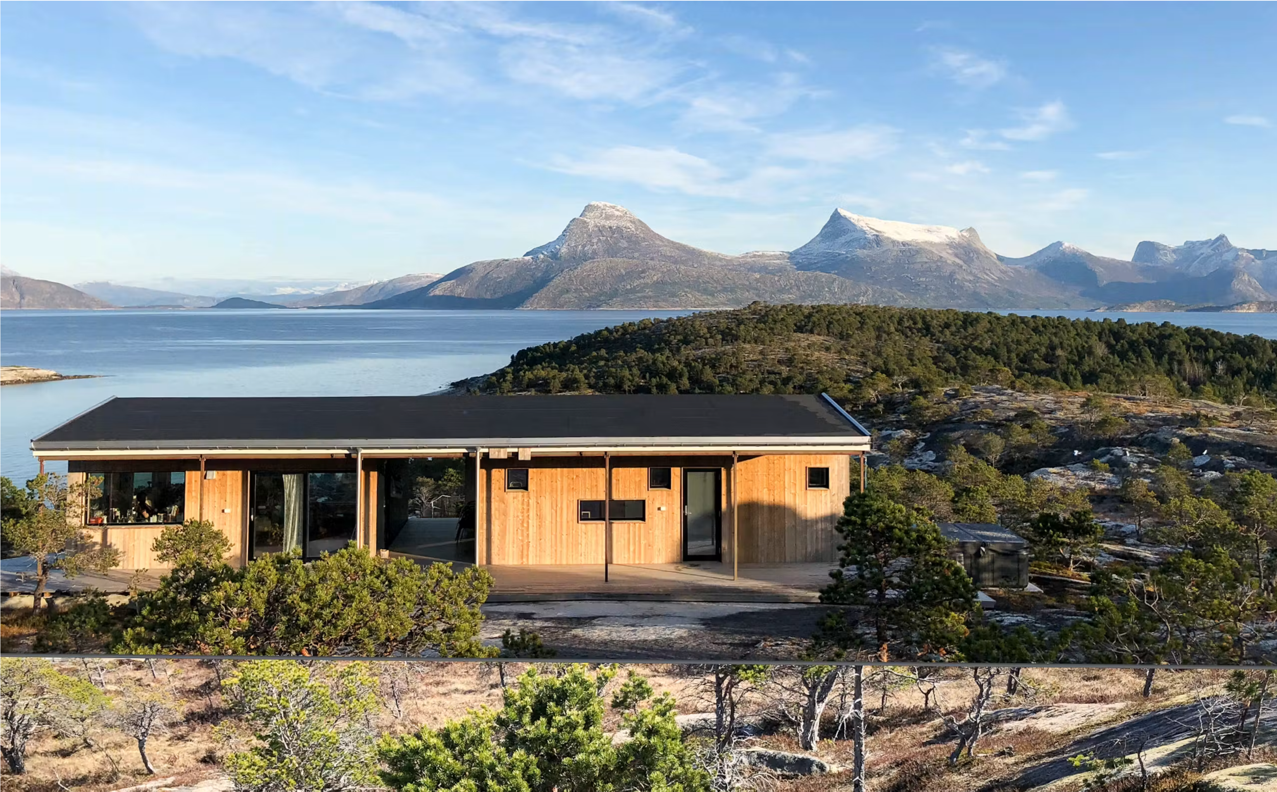 Modern wooden house with large windows overlooking a mountain lake and snow-capped mountains in the background.