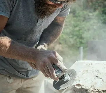 A man using an angle grinder to cut or shape a stone outdoors.