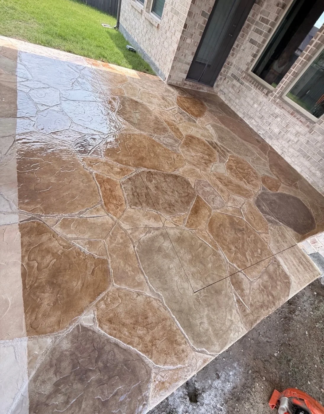 Newly installed stone patio in front of a brick house with a green lawn at the edge.