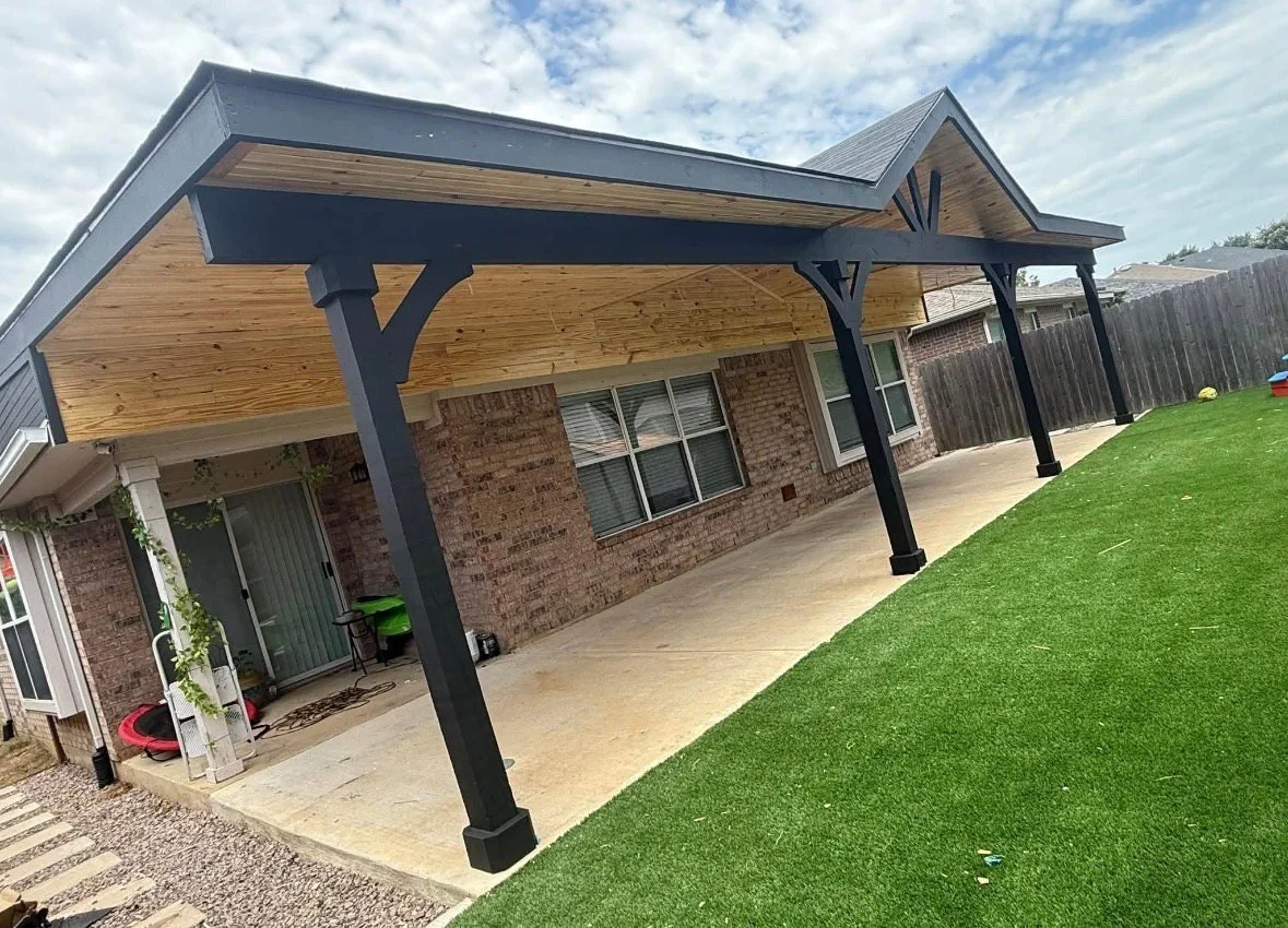 Backyard with brick house, covered patio, concrete floor, and artificial grass yard.
