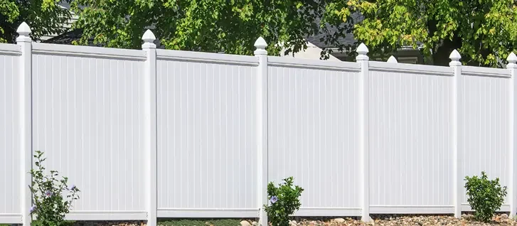 White vinyl privacy fence with some greenery and bushes in front