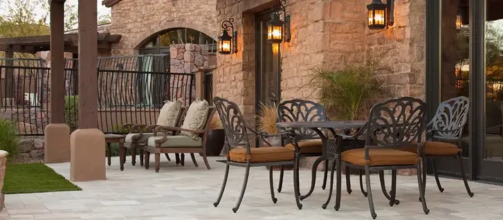 Outdoor patio with wrought iron furniture, cushion chairs, and lantern-style wall lights against a stone wall.