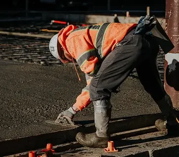 A construction worker in an orange safety jacket and helmet using a hand tool to work on railway tracks.