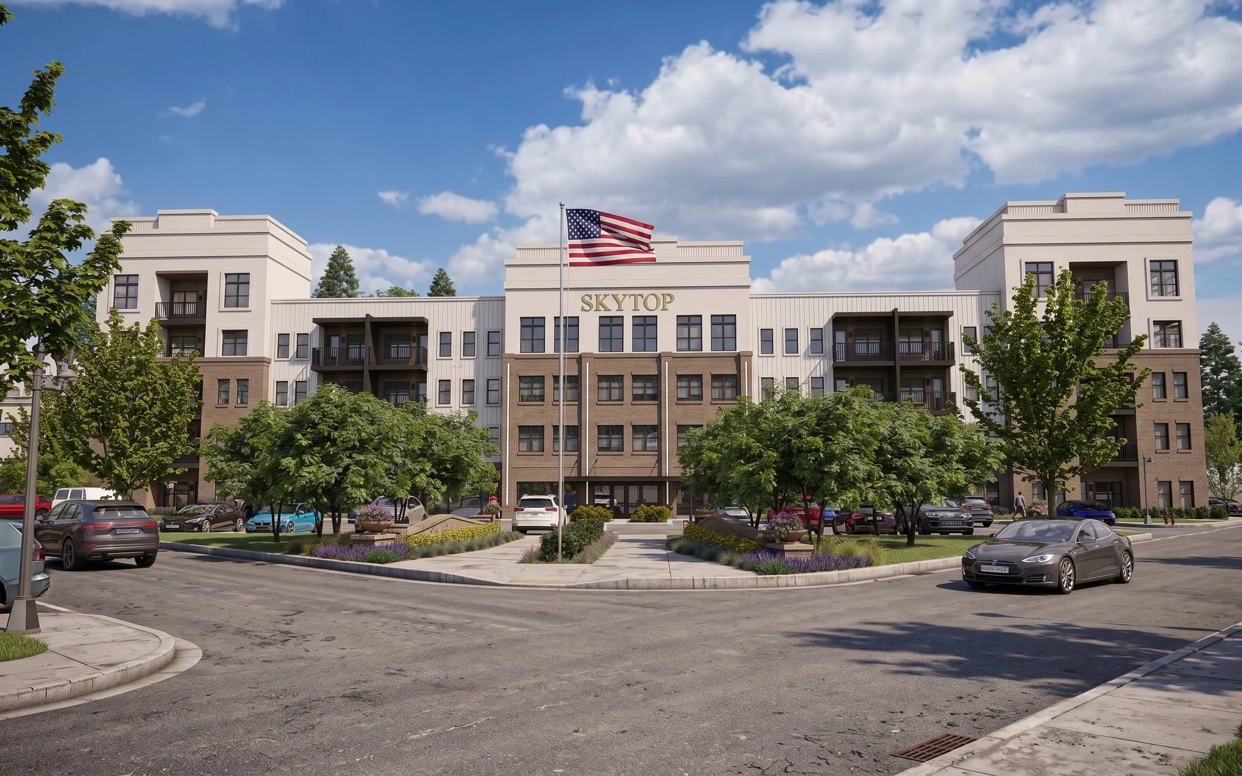 A modern multi-story residential building with the sign 'SKYTOP' on the front, an American flag flying on a flagpole, surrounded by a parking lot with several cars, green trees, and landscaped flower beds under a partly cloudy blue sky.