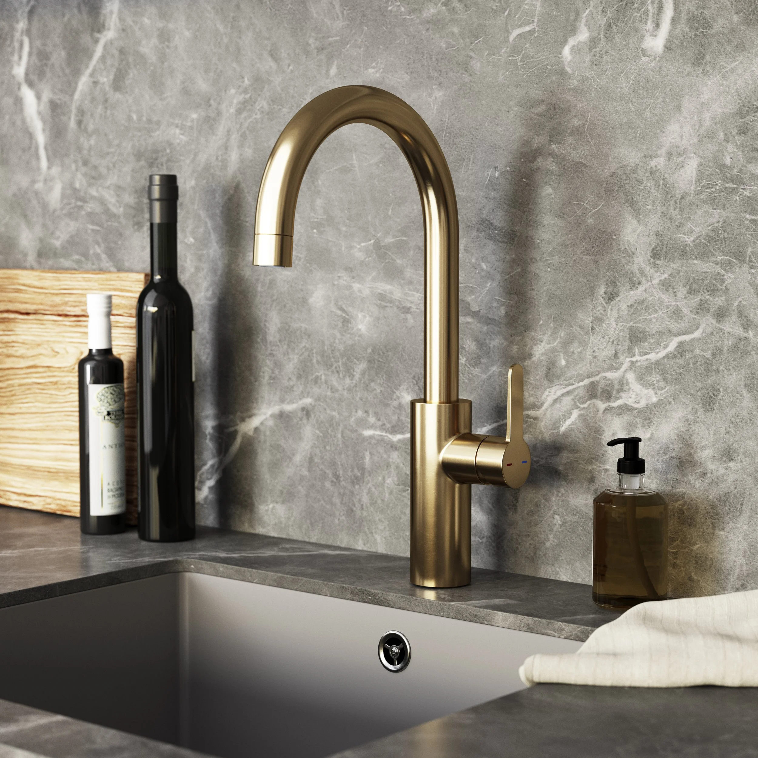 Close-up of a modern kitchen sink with a gold-colored faucet, with a soap dispenser and hand towel nearby, set against a gray marble backsplash.
