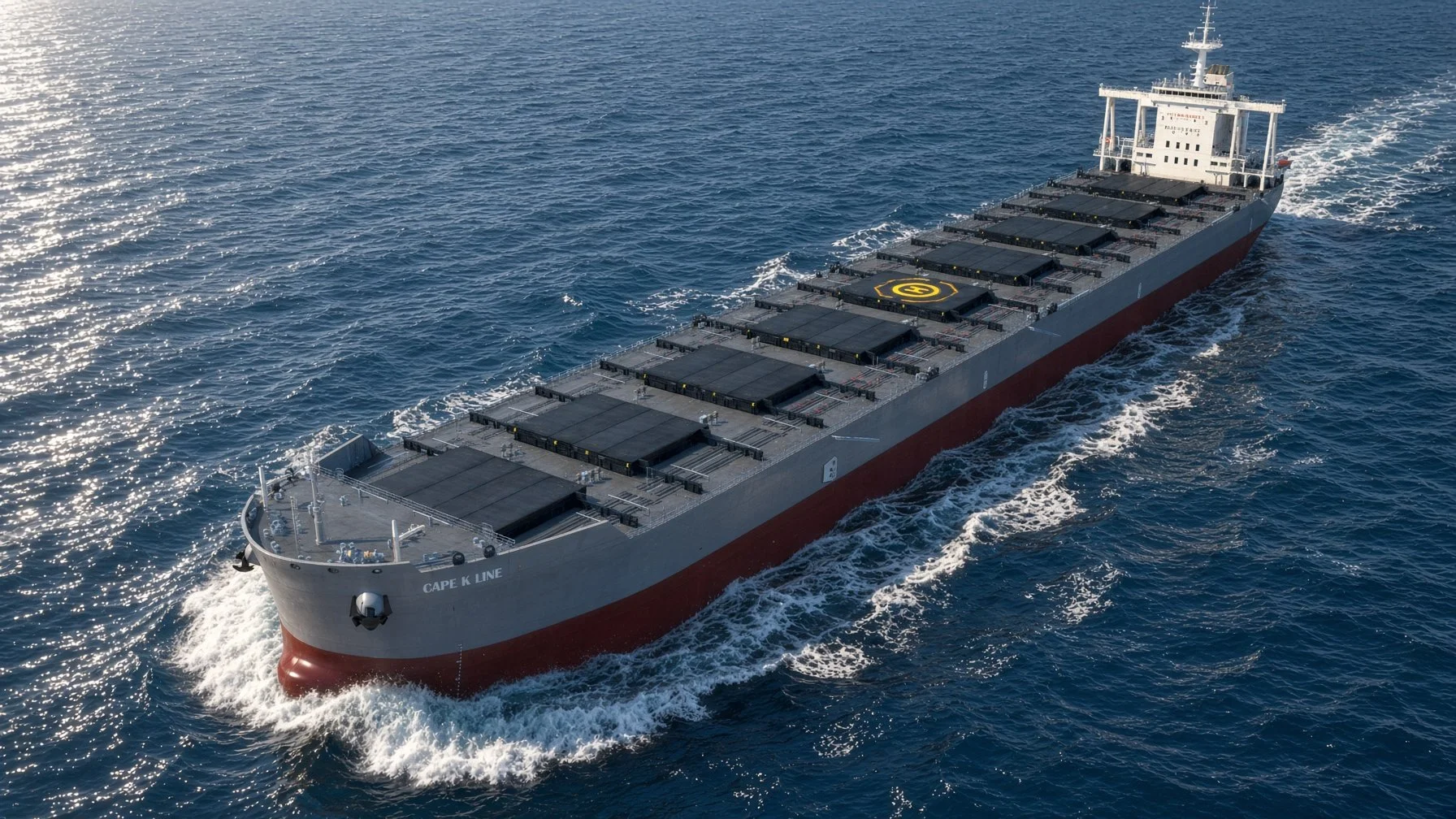 A large cargo ship sailing on the ocean, with a black helipad on the deck and white exhaust in the water behind it.