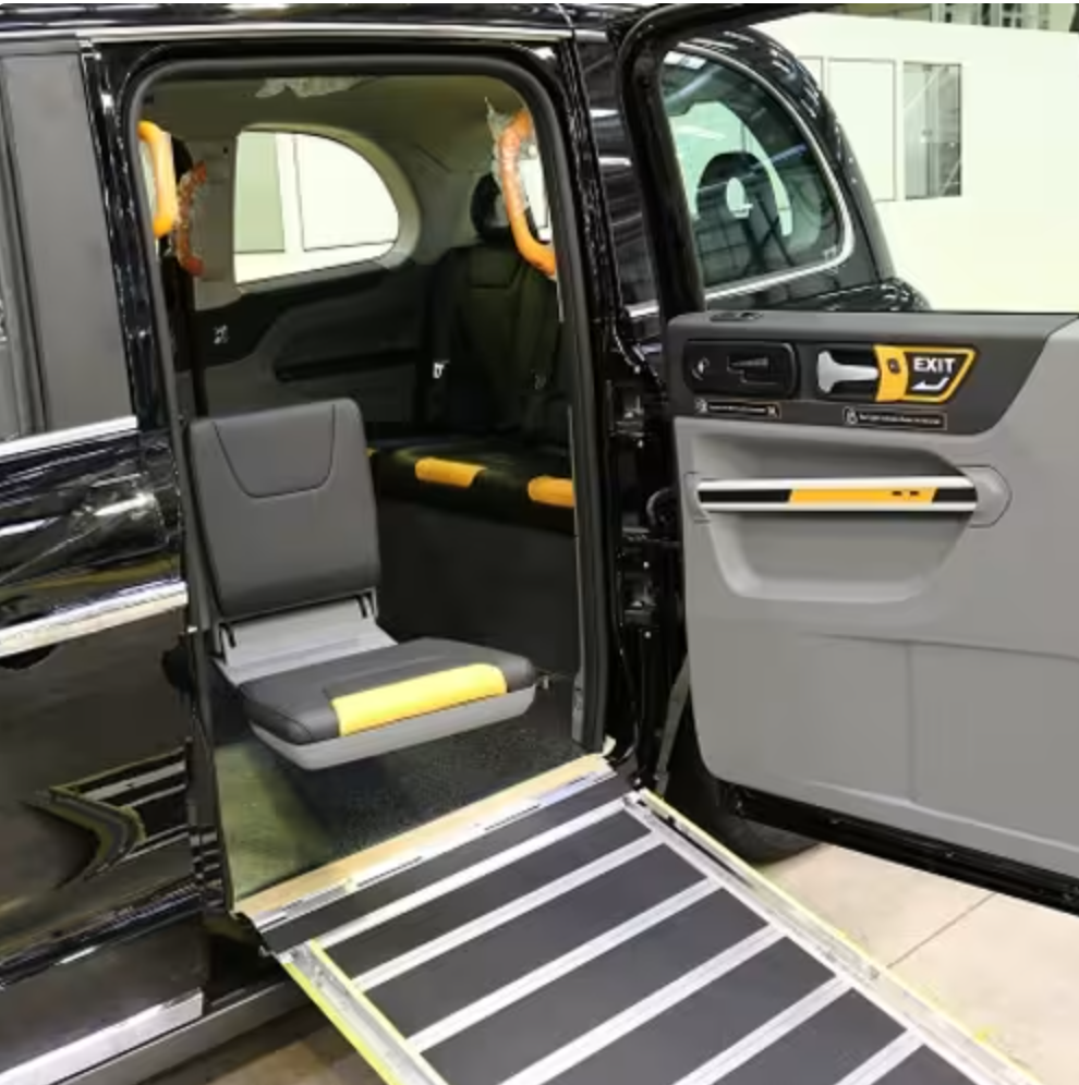 The interior of a specialized wheelchair accessible vehicle with a fold-out ramp, gray seating with yellow accents, and handrails for mobility aid.