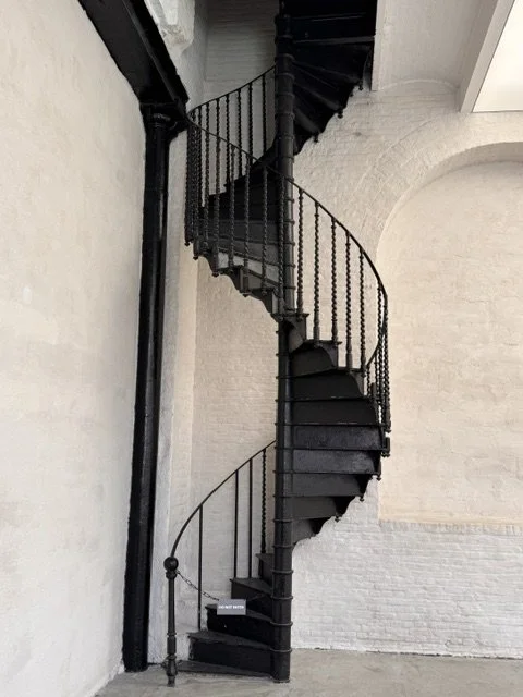 Black spiral staircase with metal railing against a white brick wall.