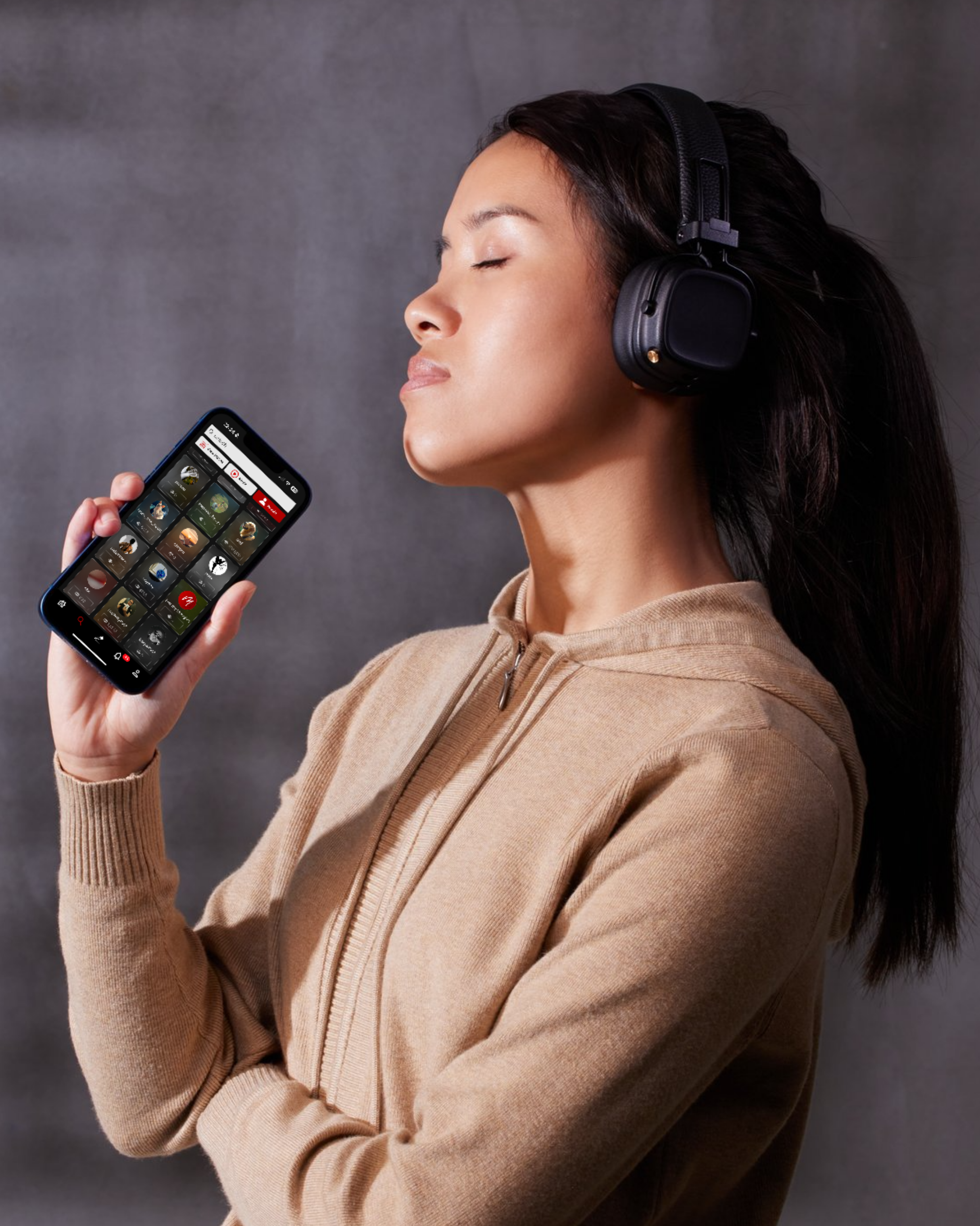 A woman with medium skin tone and long dark hair wearing a beige zip-up hoodie, glasses on her head, and large black over-ear headphones, holding a smartphone with a food delivery app open.