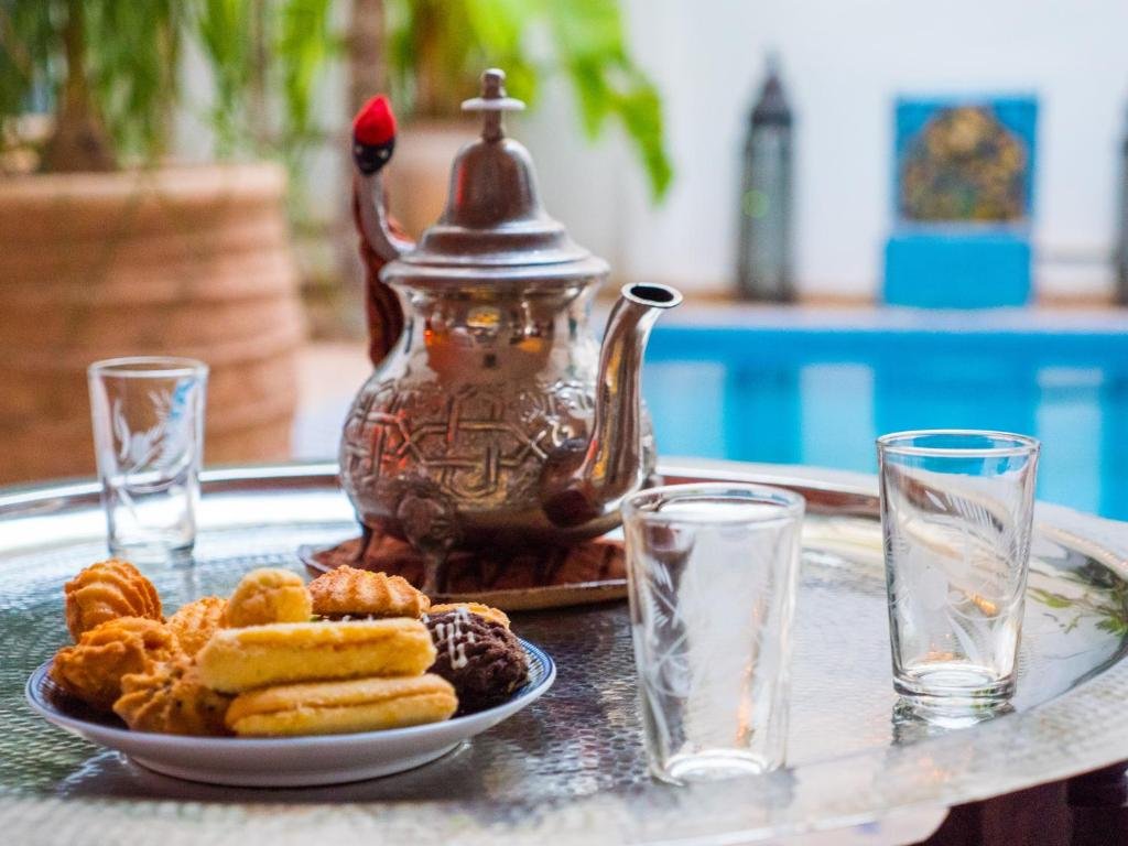 A tray with a teapot, three glasses, and a plate of assorted cookies, with a blurred background of plants and a swimming pool.