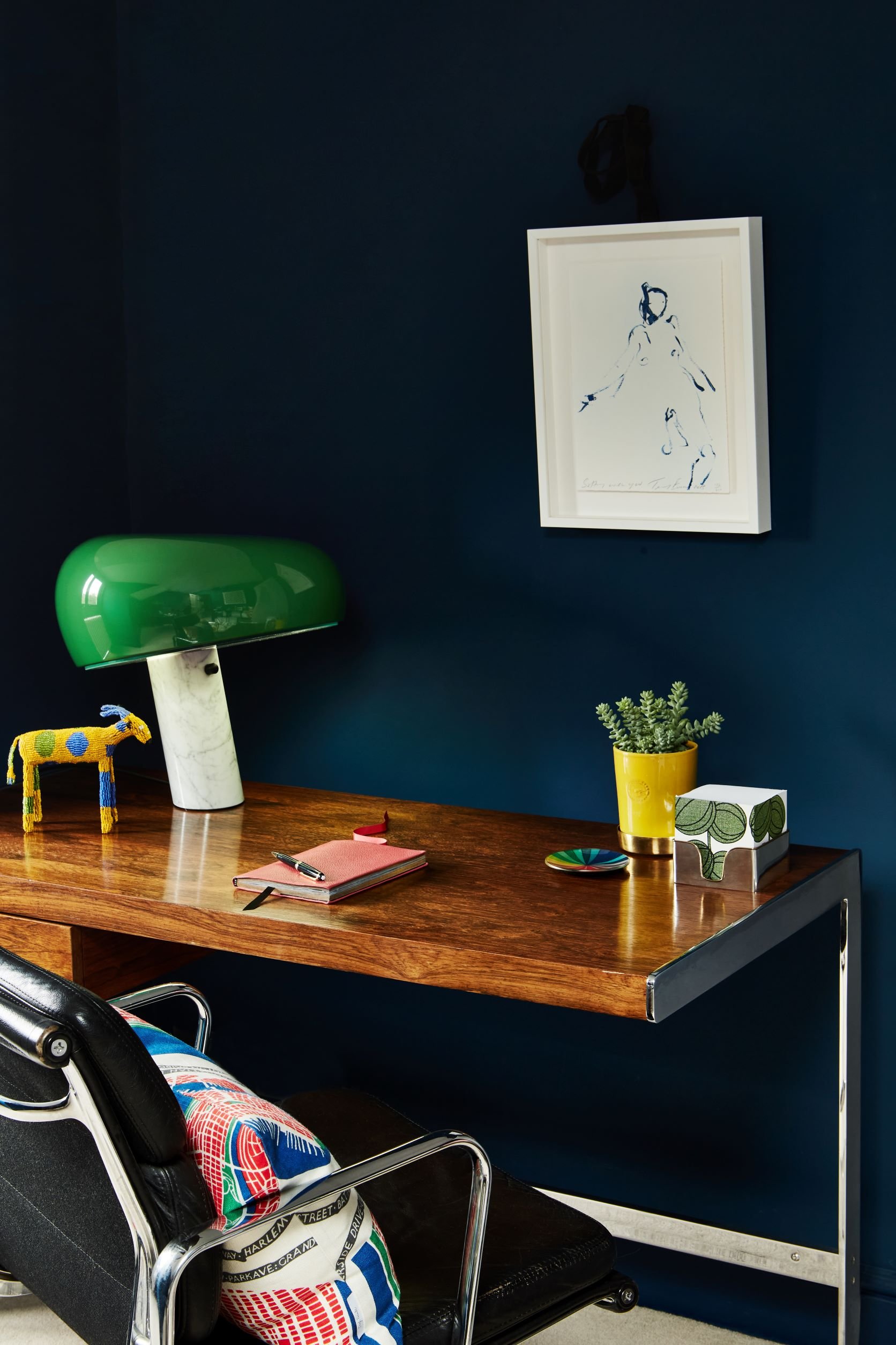 Dark, inky blue home office with a mid-century rosewood desk, Flos Snoopy Table lamp, Eames office leather chair, art work