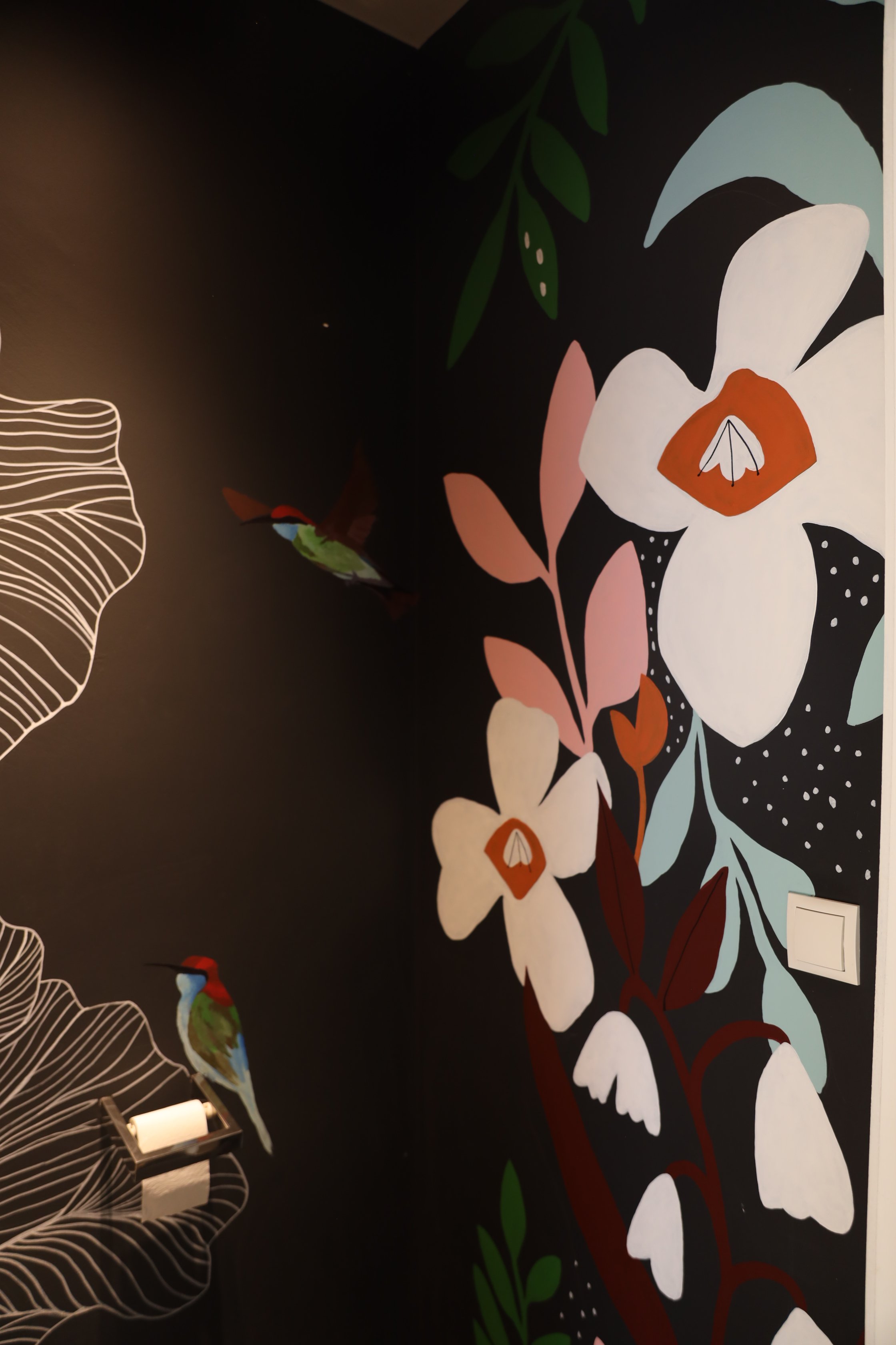 Colorful floral mural on a dark wall, featuring white, pink, and orange flowers with green leaves and abstract patterns.