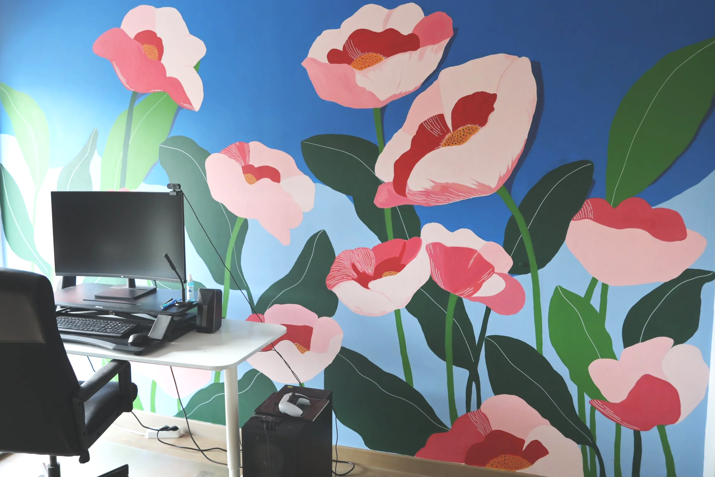 Office workspace set against a vibrant mural of large pink and red flowers with green leaves on a blue background.