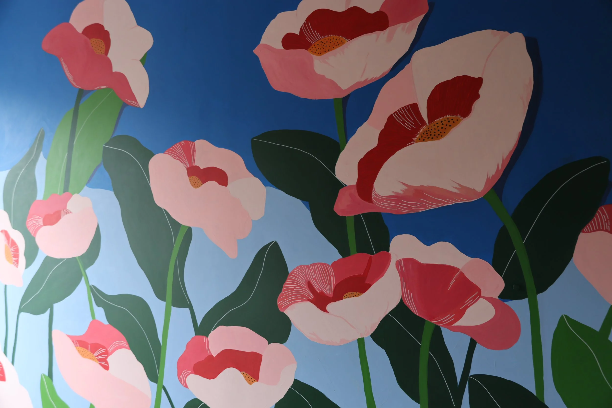 A vibrant mural of pink and red poppy flowers with green leaves against a blue background.