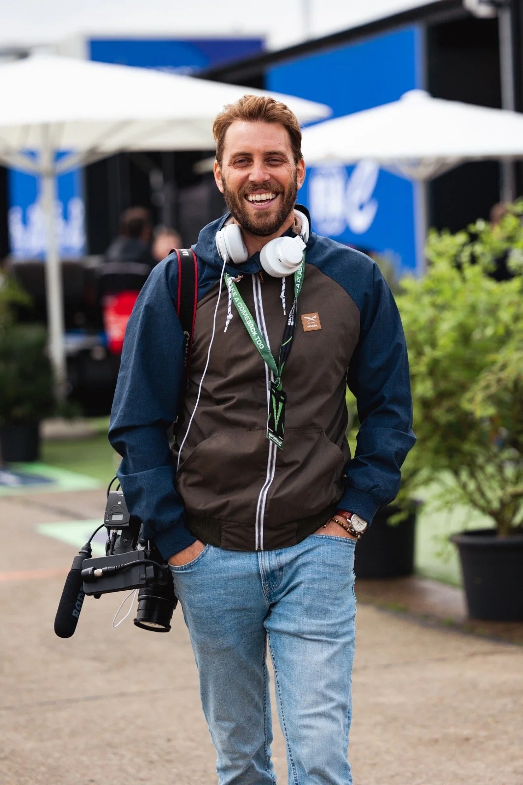 Un vidéaste souriant porte une caméra et marche dans un environnement extérieur.