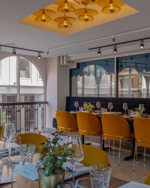 Interior of Conversate Steak & Seafood in Hamilton featuring yellow chairs and a large window,