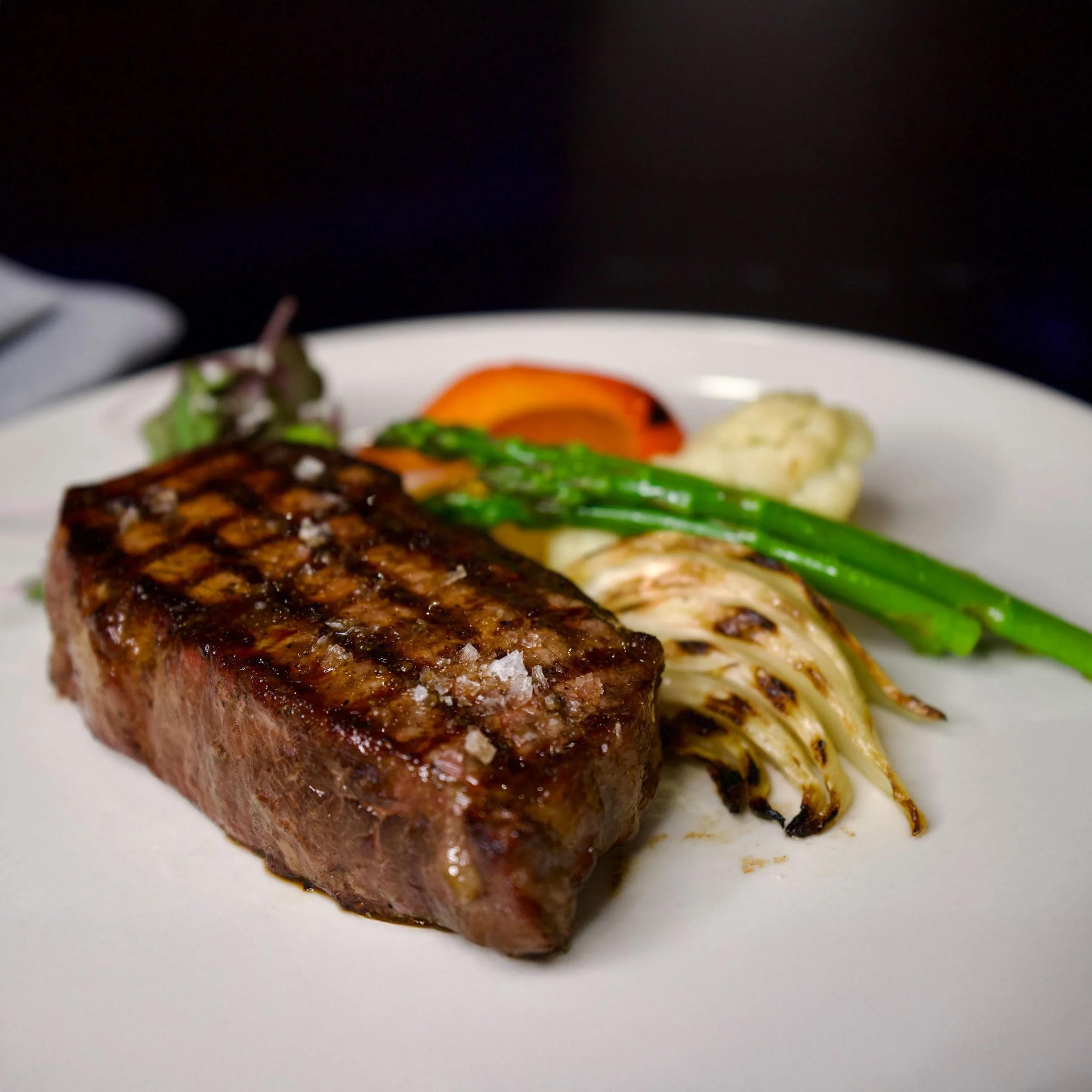 Steak served with roasted vegetables and greens on a white plate at Conversate Steak & Seafood in Hamilton.
