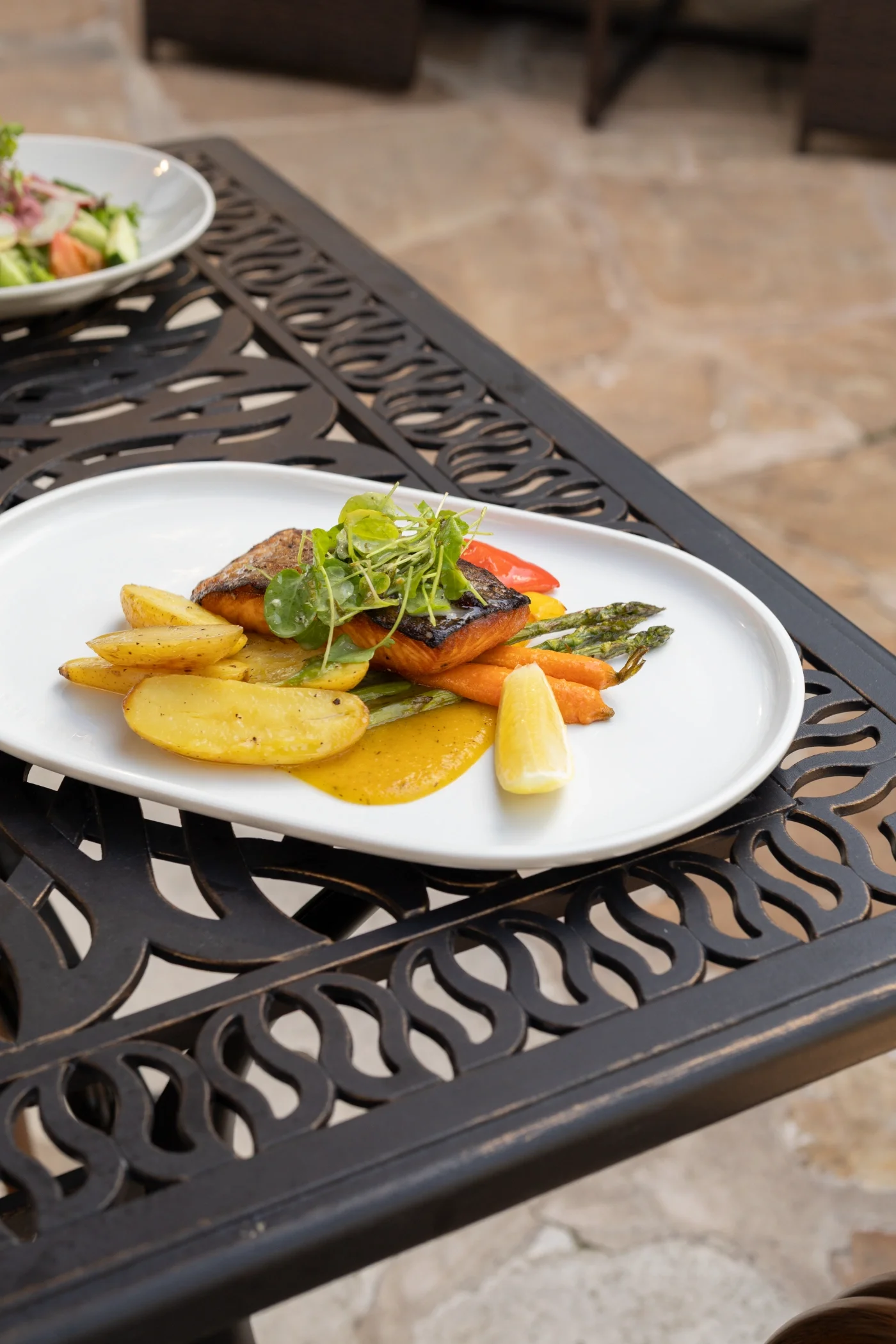 Plate of grilled salmon with accompaniments on a decorative black outdoor table