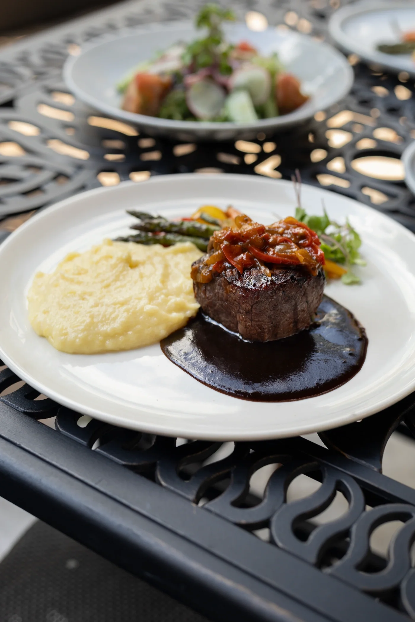 A plate with mashed potatoes and steak on a black outdoor table.