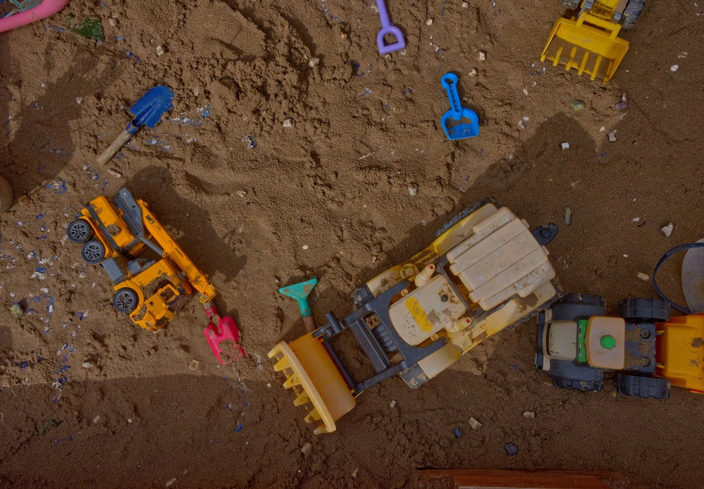 Children's outdoor sandbox filled with toy construction vehicles, shovels, and sand.