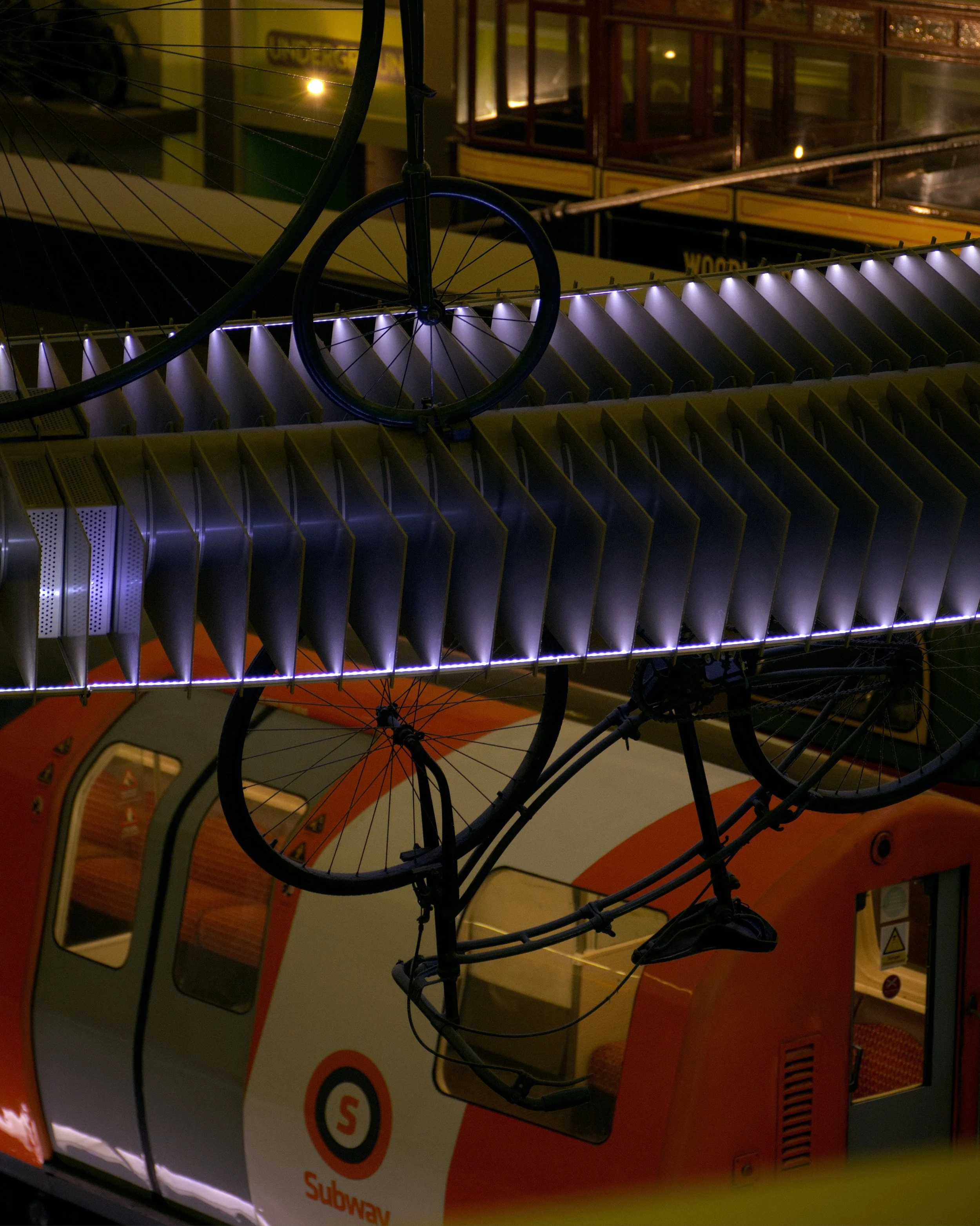 Close-up of a miniature bicycle mounted on top of an orange and white Glasgow subway train, with a yellow and black sign in the background at Glasgow Transport Museum.
