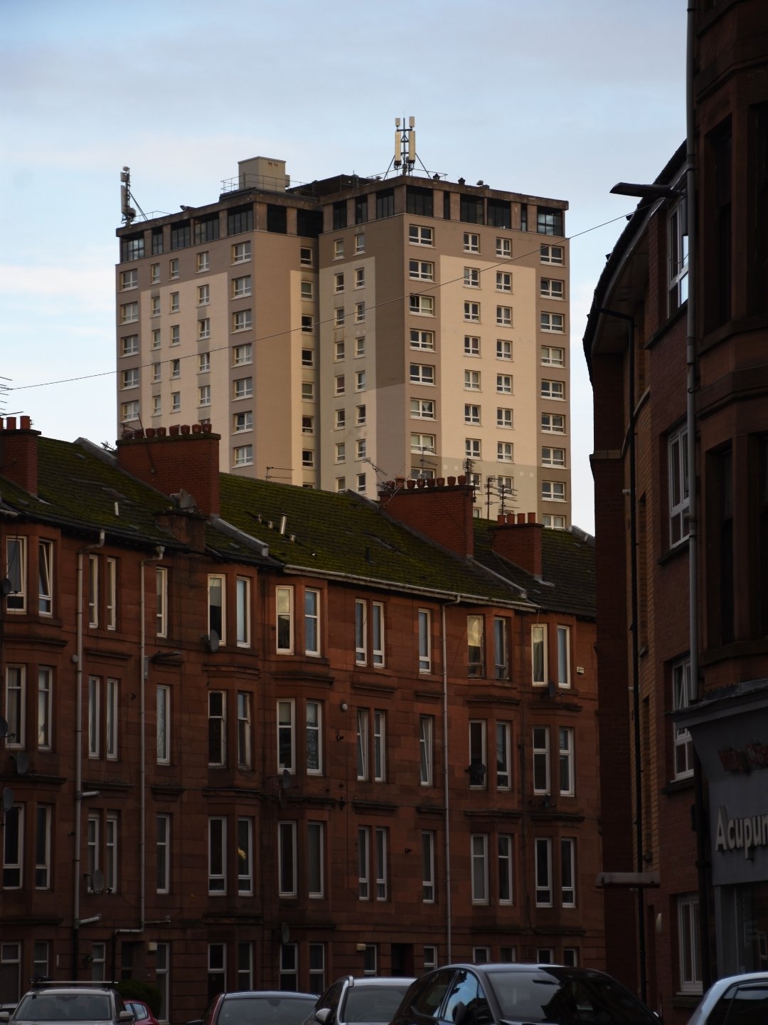 A cityscape with old red brick buildings in the foreground and a tall beige apartment building in the background under a cloudy sky.