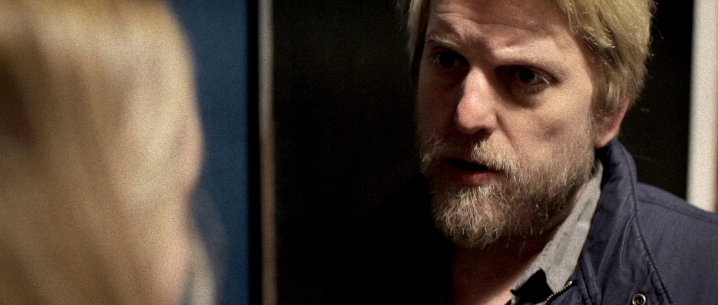 A man with blonde hair and a beard looks intently at someone off-camera, mid-conversation.