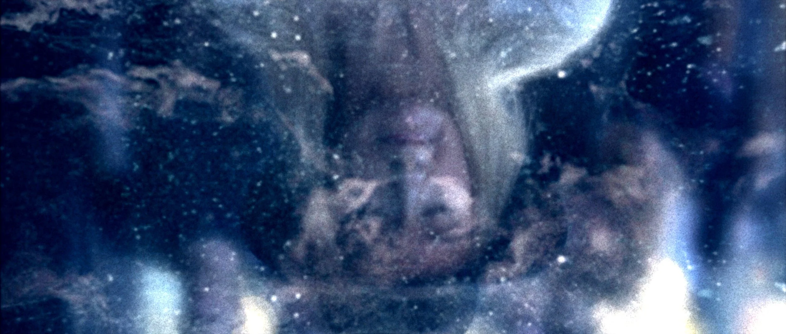 A person with dark curly hair is surrounded by swirling cosmic clouds and stars, giving an ethereal, galaxy-like appearance.