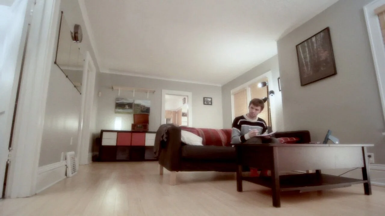 Young man sitting on a couch in a living room reading a book or magazine.