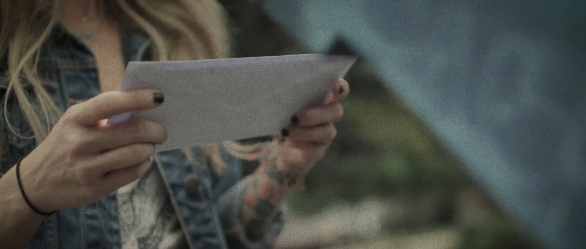 Close-up of a person with long hair holding a smartphone or tablet device with both hands. The person is wearing a plaid shirt or jacket.