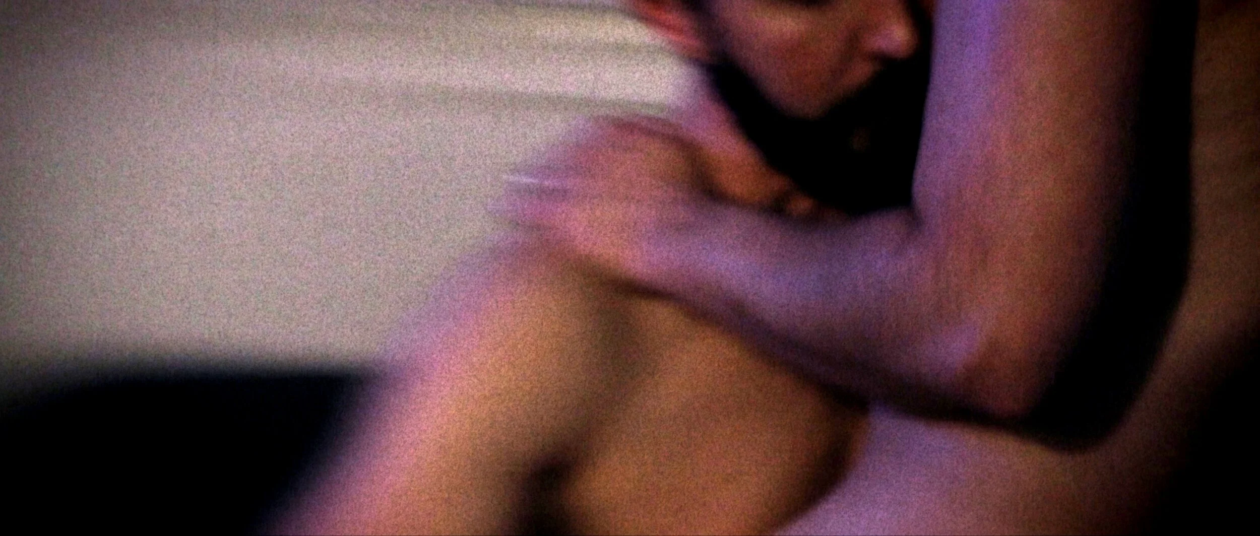 A close-up of a person with a dark background, partially visible facial features, and an arm, in a dimly lit setting.