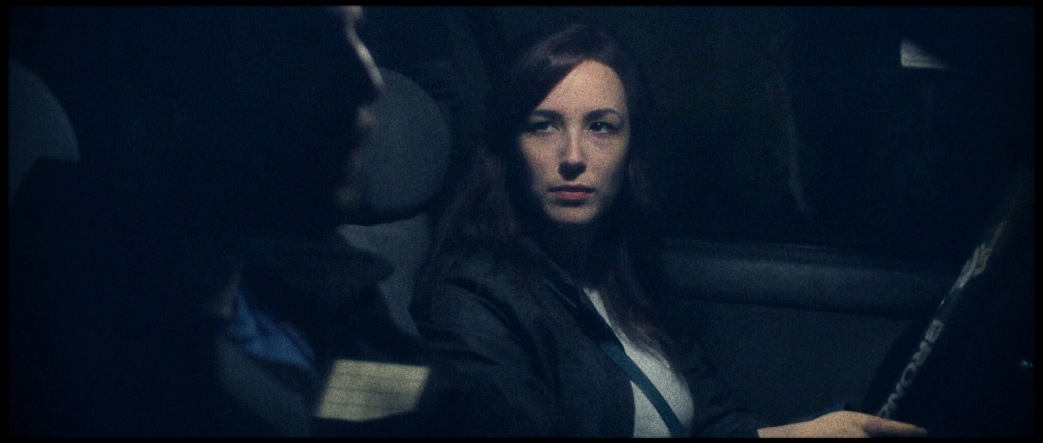 A woman with long brown hair sitting in a car, looking at a person with short hair who is driving.