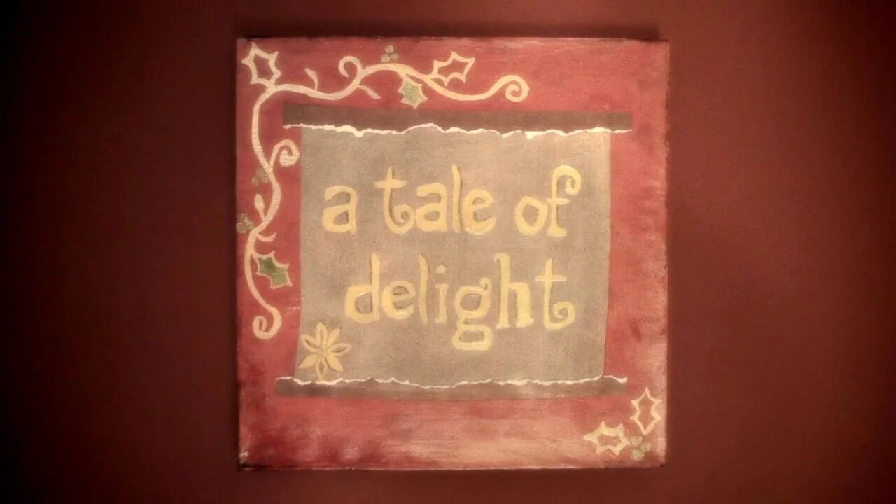 Decorative holiday sign with the words "a tale of delight" written inside a festive border with holly and a poinsettia design.