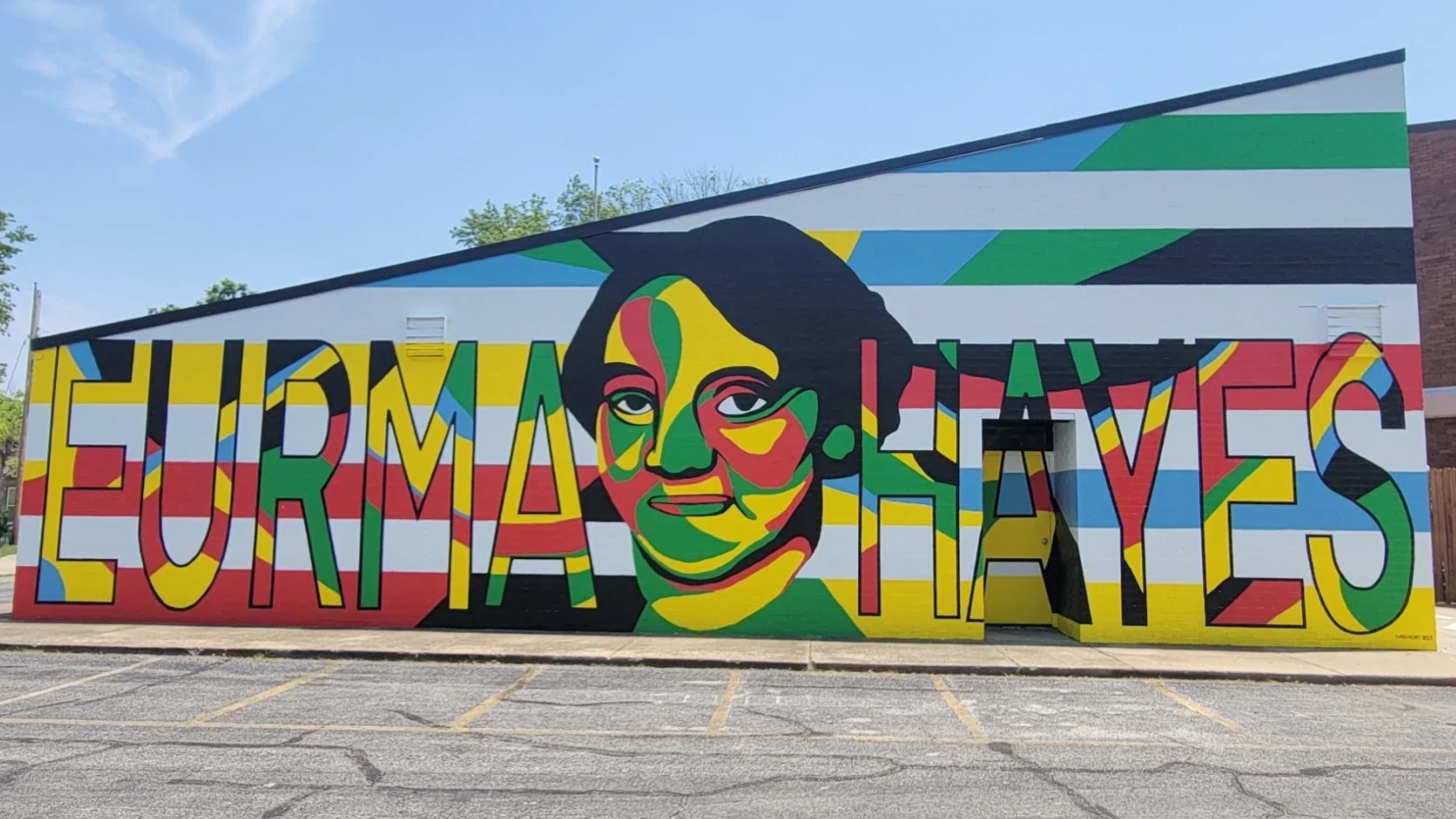 Colorful mural with the words 'Eurama Hoyes' and an abstract portrait of a woman with large eyes, painted in bright colors including red, green, yellow, blue, and black, on a building wall.