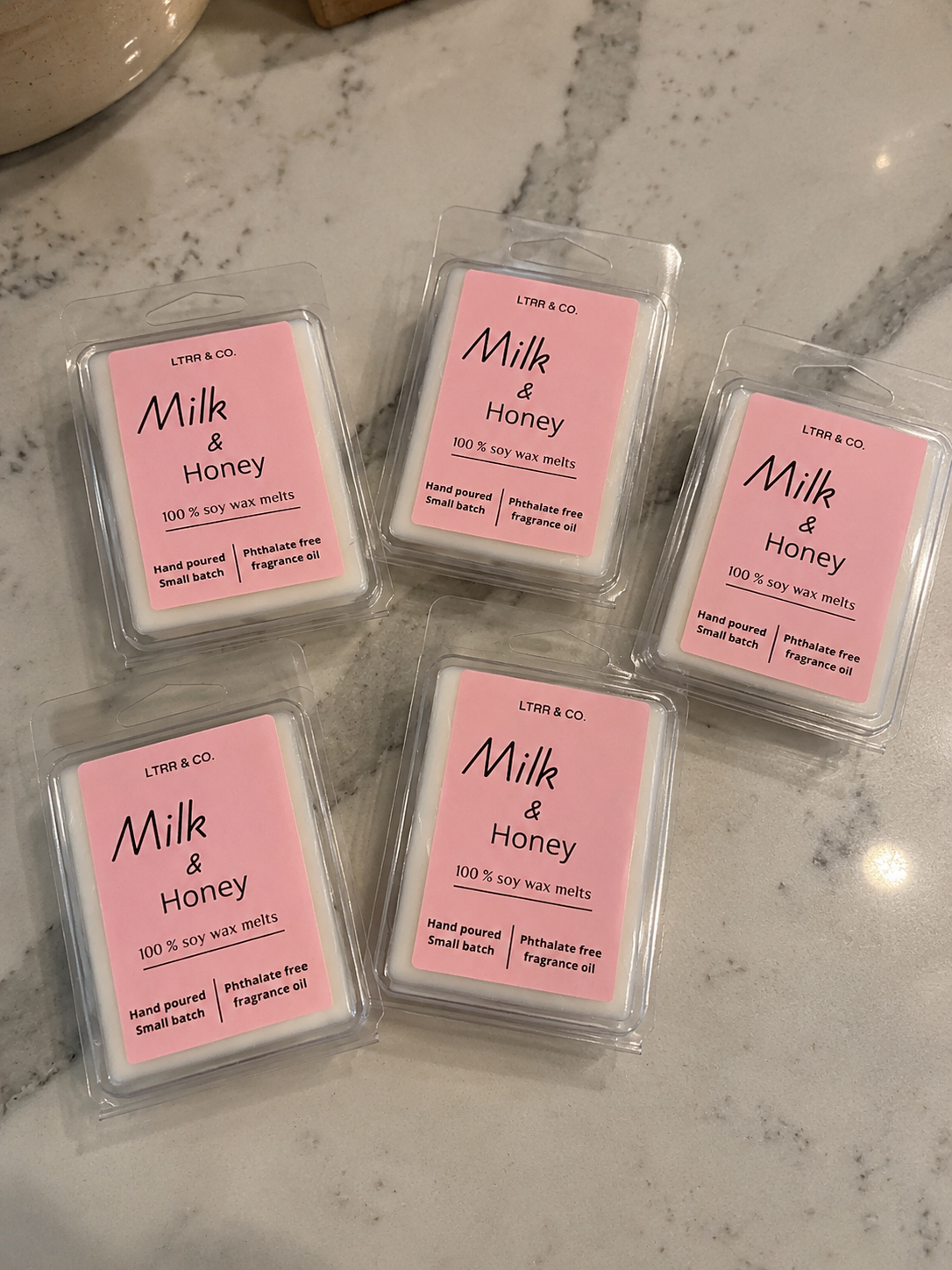 Five bars of soy wax melts labeled 'Milk & Honey' with pink packaging, placed on a white marble surface.