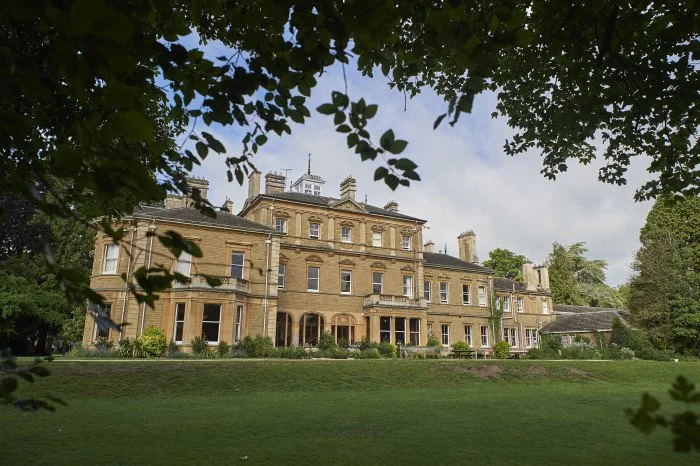Bruern Abbey School, a Victorian stone country house seen across its lawn, framed by trees