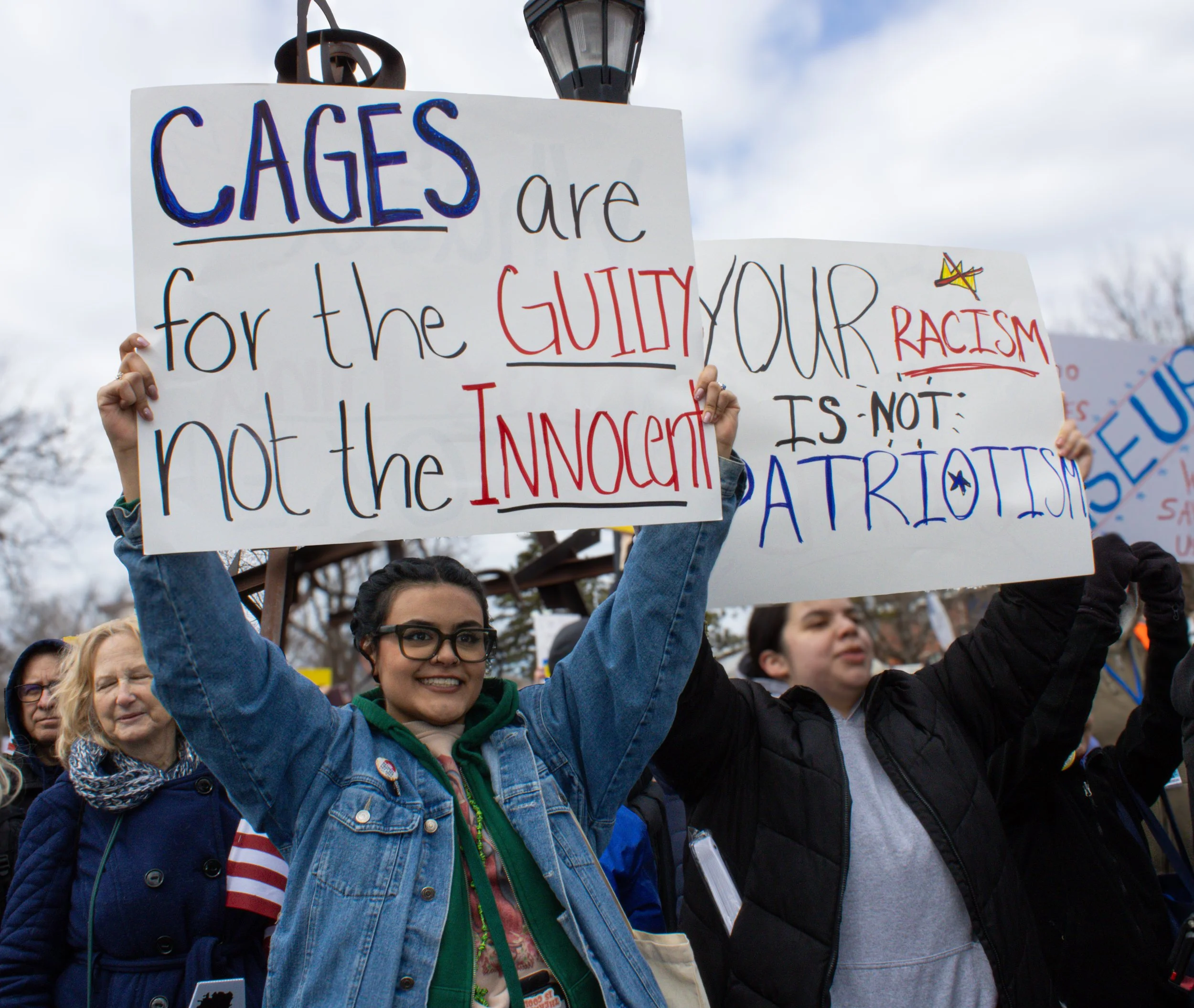 A group of protesters holding signs, with one sign reading 'CAGES are for the GUILTY, NOT the INNOCENT', during a demonstration outdoors on a cloudy day.