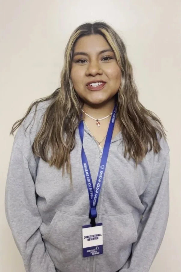 Young woman with wavy hair wearing a grey hoodie and a blue lanyard with a badge that says 'Constitutional Observer'.