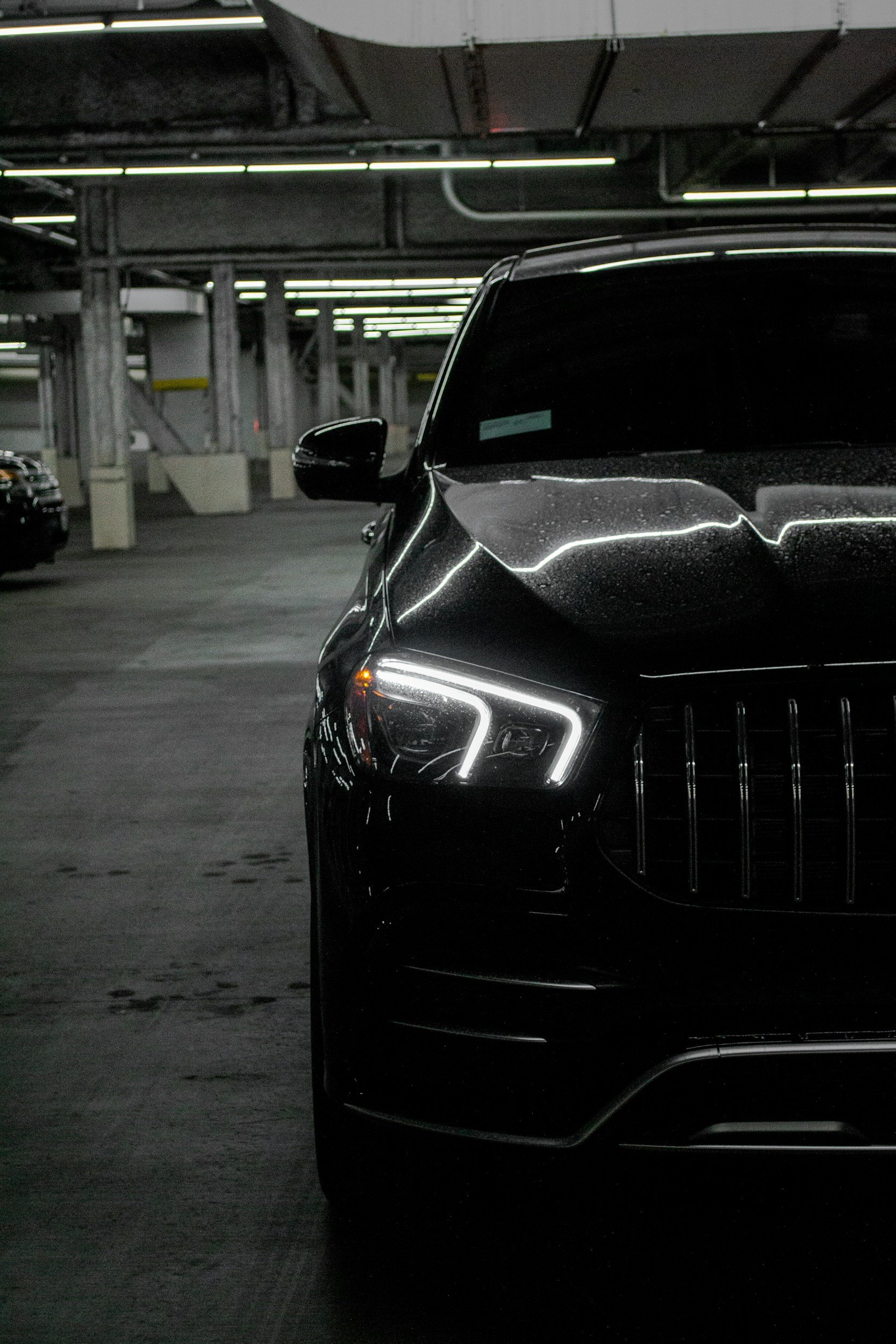 Voiture noire dans un parking souterrain avec des lumières suspendues au plafond.