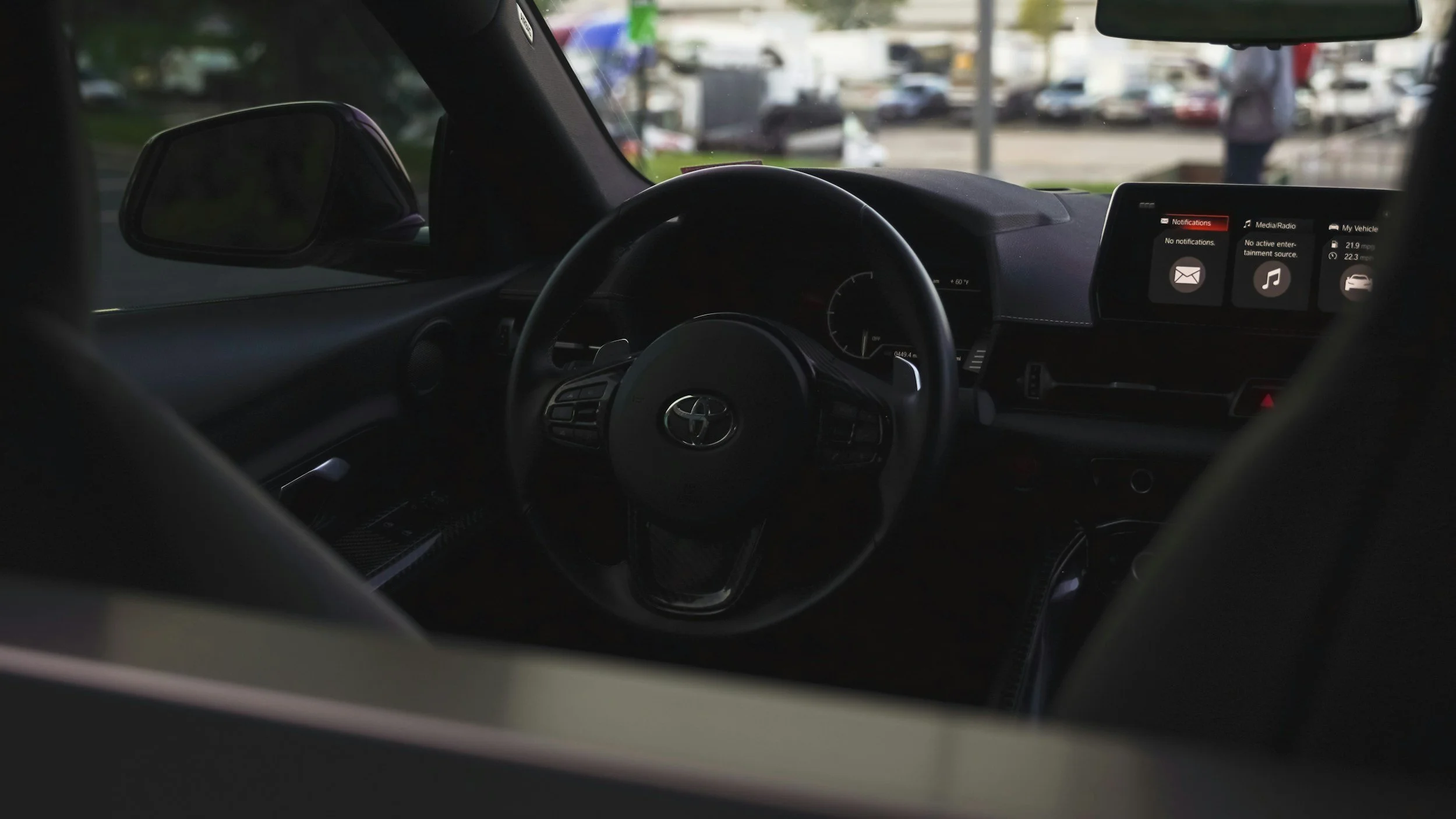 Intérieur d'une voiture avec tableau de bord digital, volant avec logo Toyota, et écran d'infodivertissement affichant des notifications et des icônes.