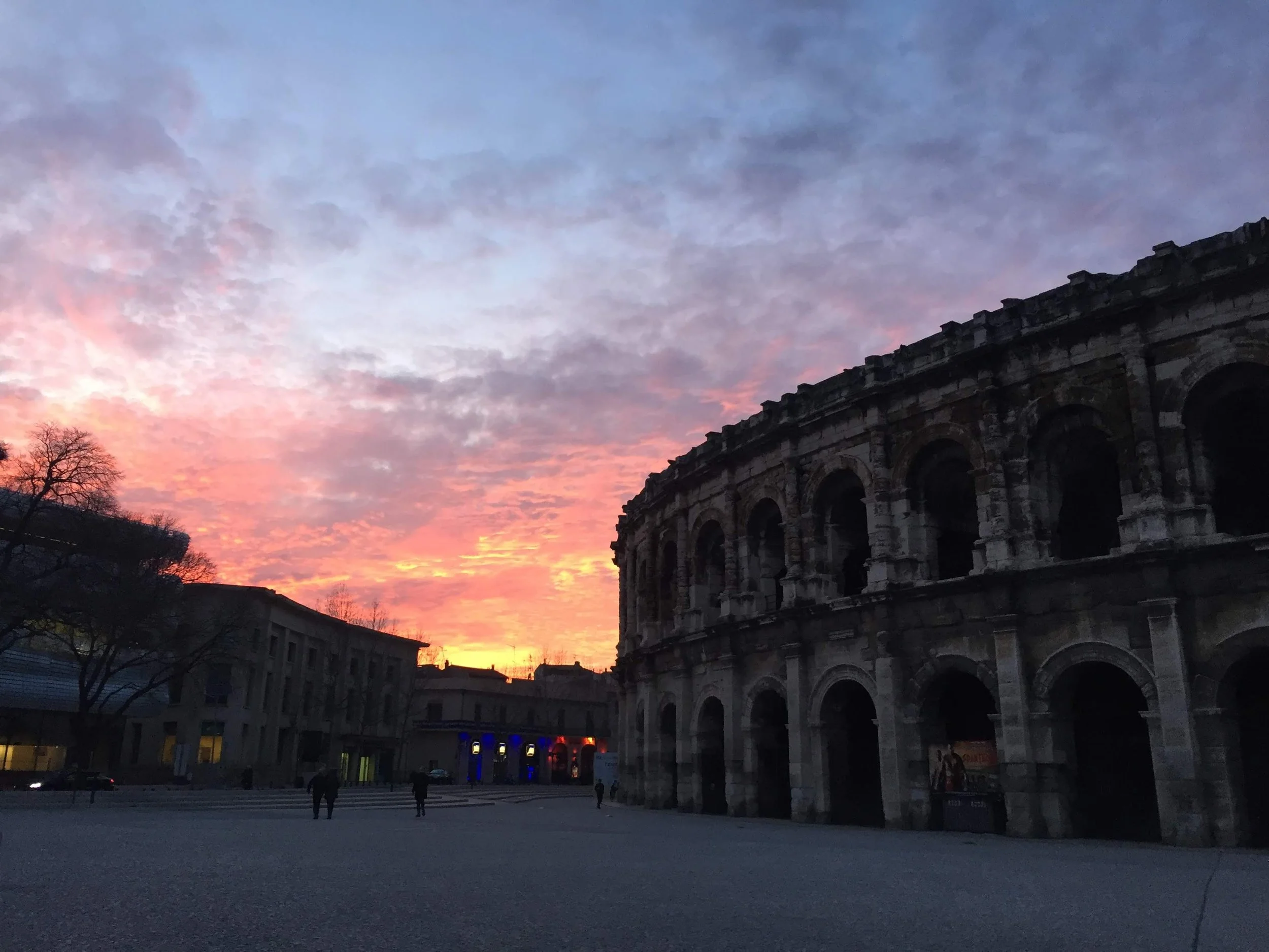 Les Arènes de Nîmes sous un ciel coloré au coucher du soleil.