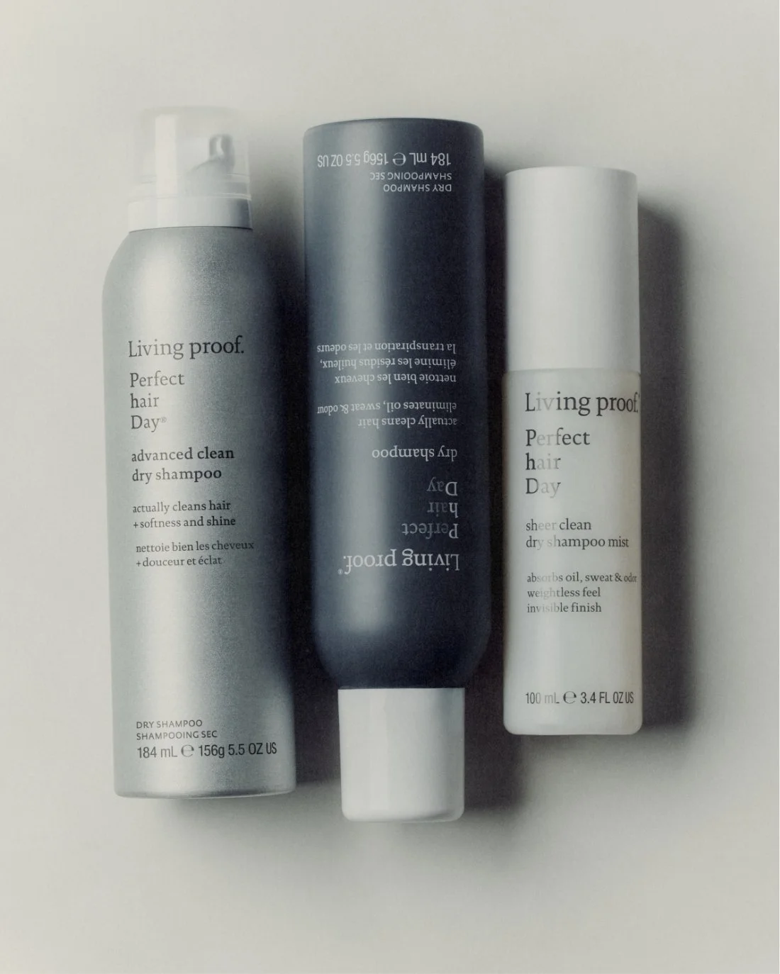 Three hair care products from Living Proof: a silver bottle of dry shampoo, a dark bottle of dry shampoo, and a white bottle of dry shampoo mist.