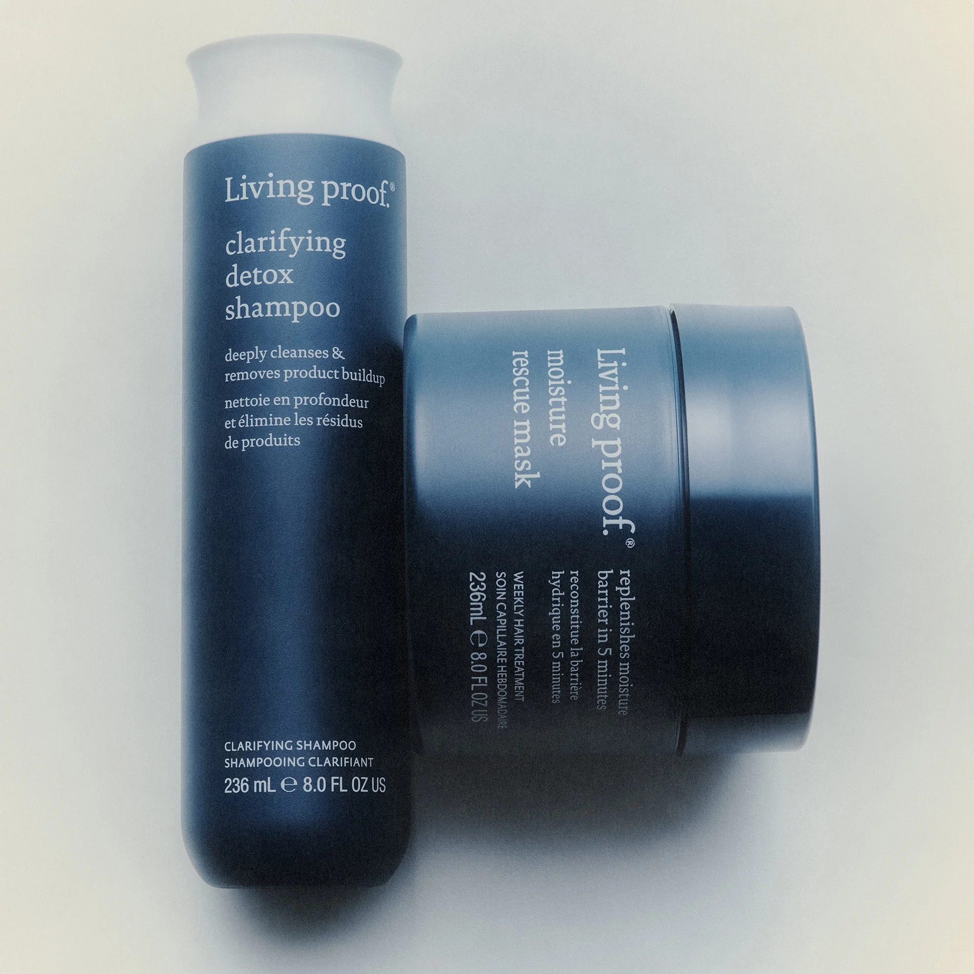 A blue bottle of Living Proof clarifying detox shampoo lying on a neutral surface, with part of another similar bottle visible beside it.