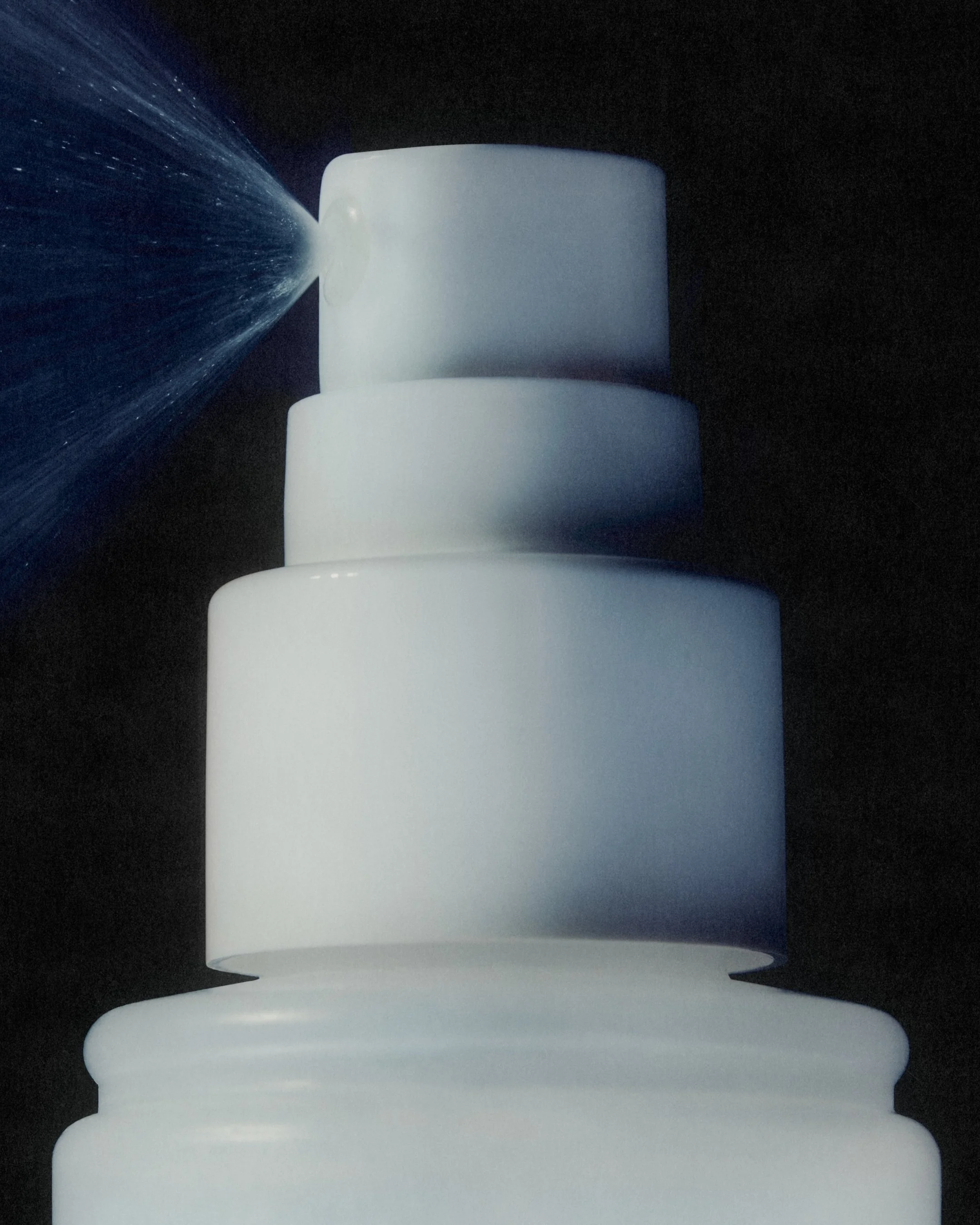 Close-up of a white nozzle spraying water onto a white toilet paper roll in a dark environment.